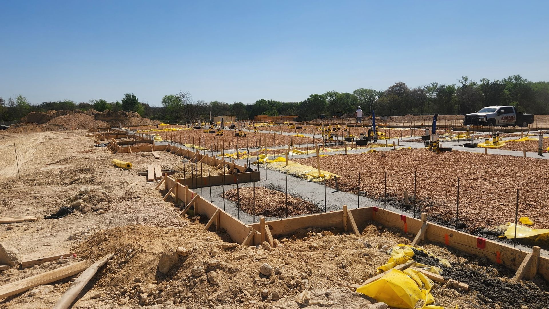 Construction site with wooden foundation forms and yellow sand under a clear sky