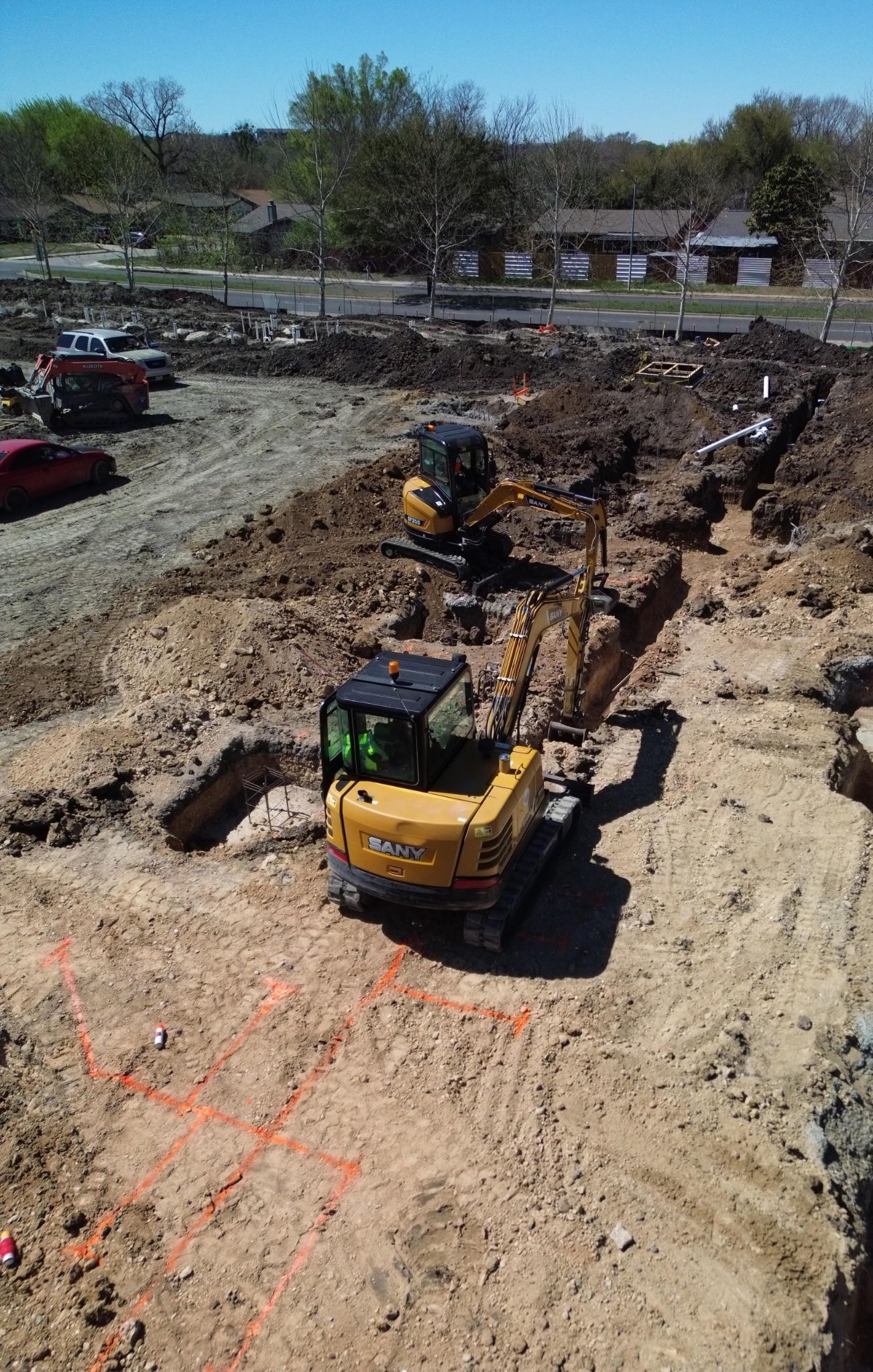 Construction site with two yellow excavators digging a long trench under a clear sky