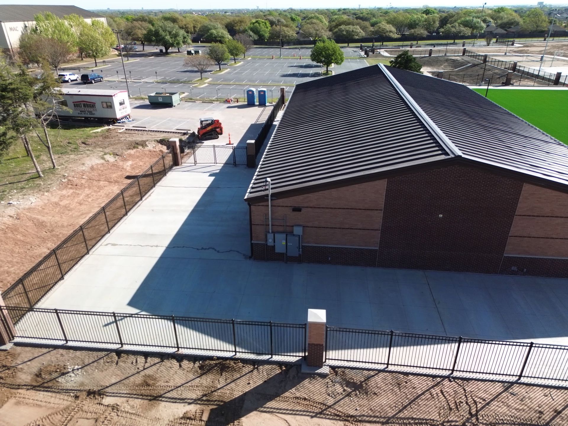 Aerial view of a modern building with a black striped roof beside an empty paved lot and parked vehicles.