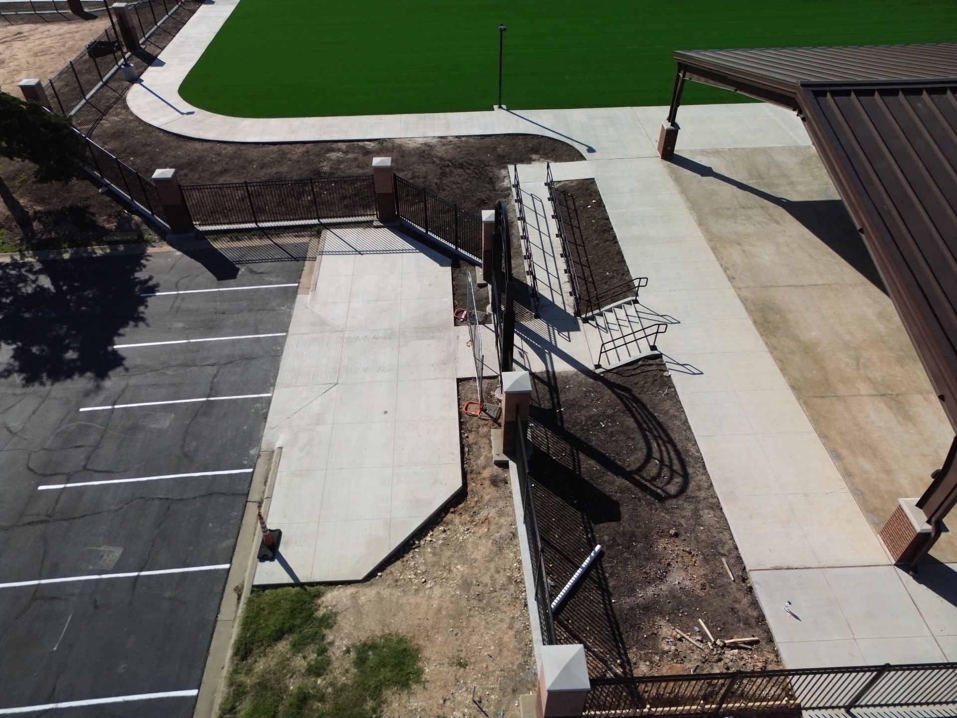 Aerial view of a walkway and parking lot beside a green sports field, with ramps and a covered area