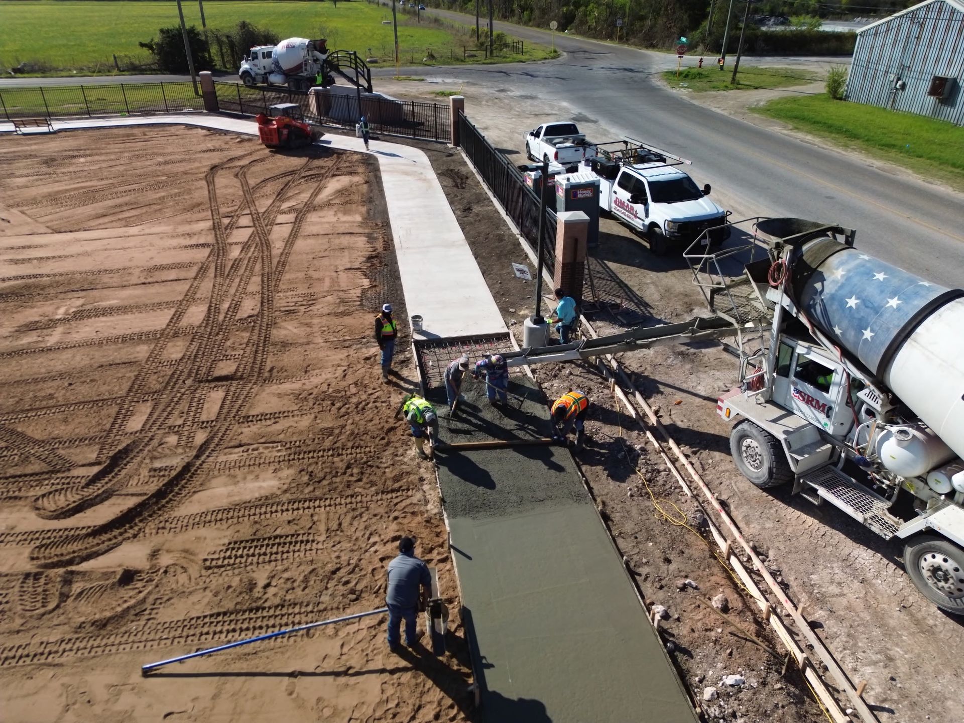 Construction crew paving a new roadside path beside parked trucks and a cement mixer