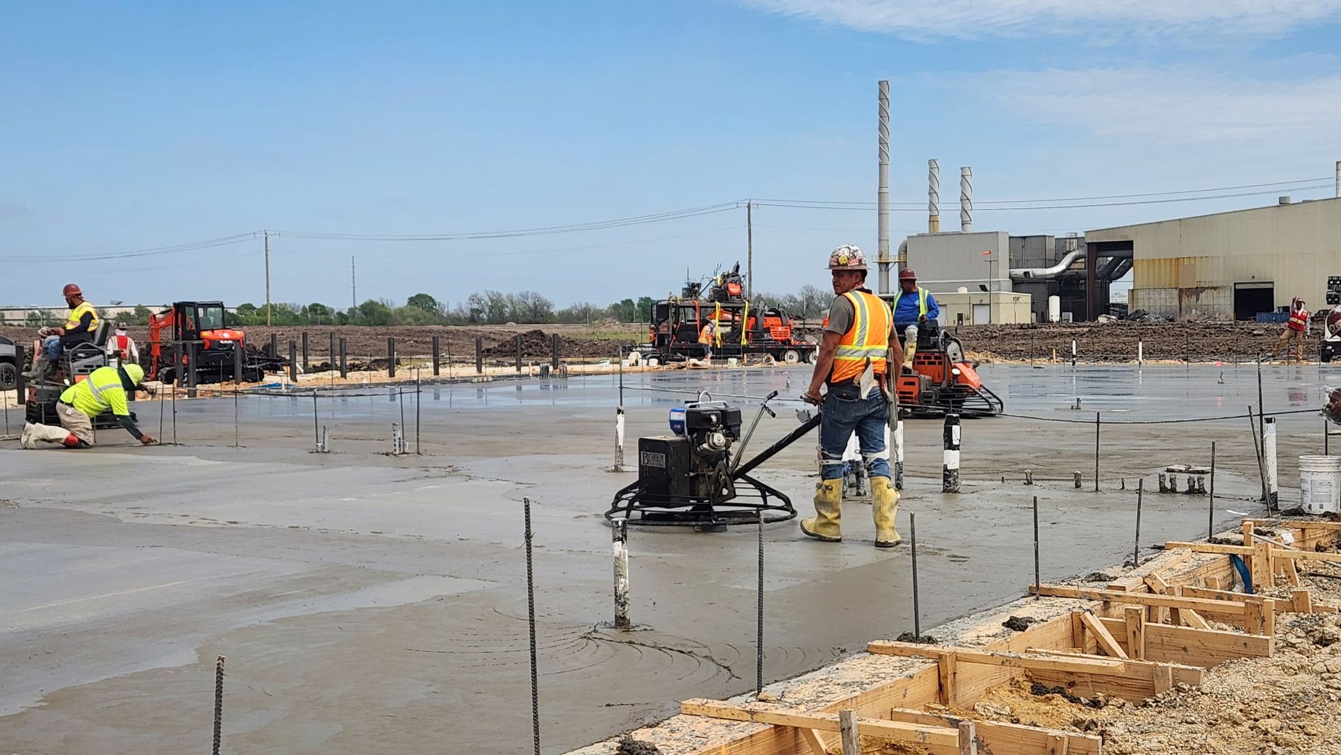 Construction workers pouring a concrete slab at a building site with rebar and equipment in the foreground
