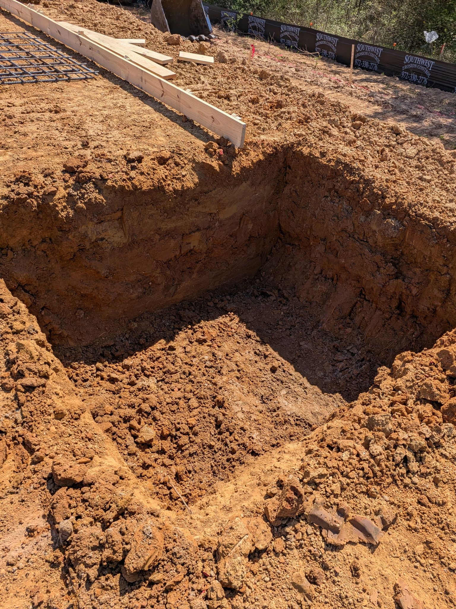 Freshly dug rectangular trench in reddish soil at a construction site