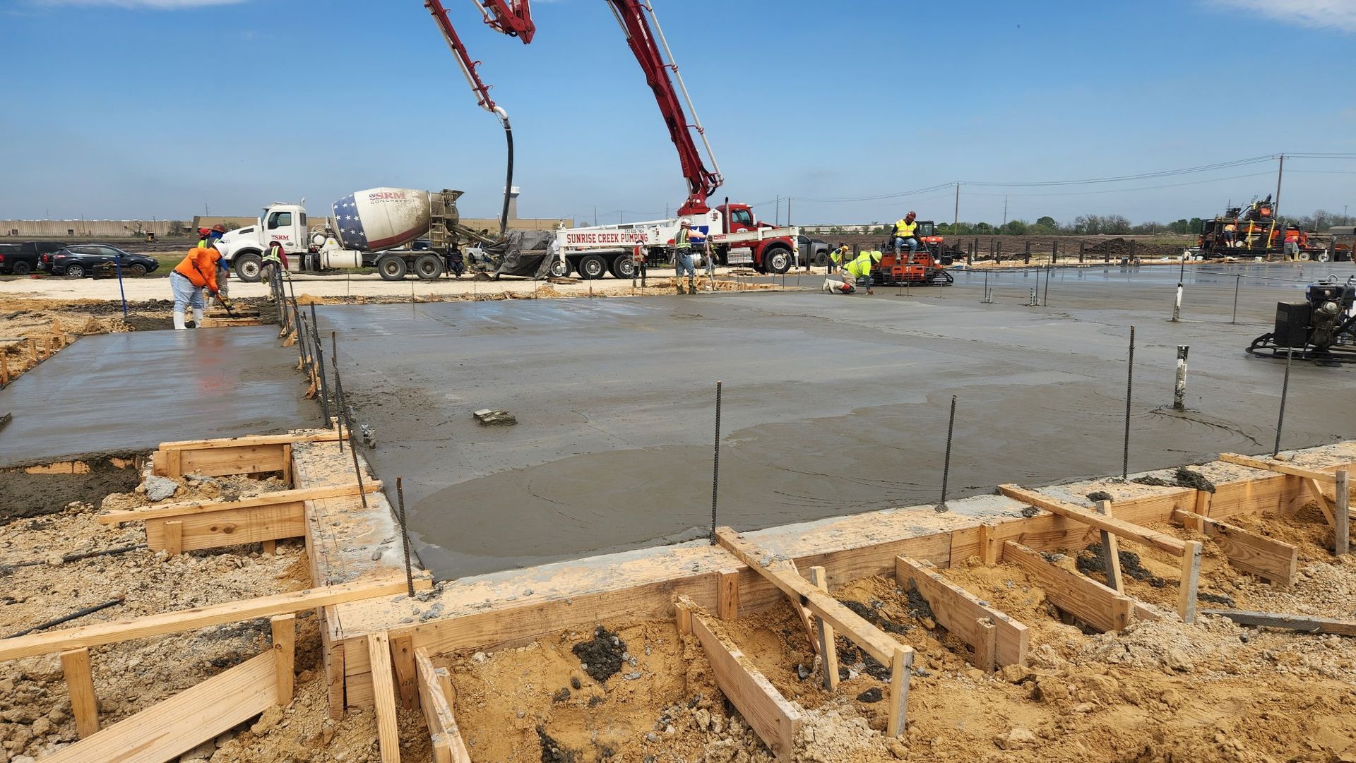 Concrete foundation being poured at a construction site with cranes and workers in the background