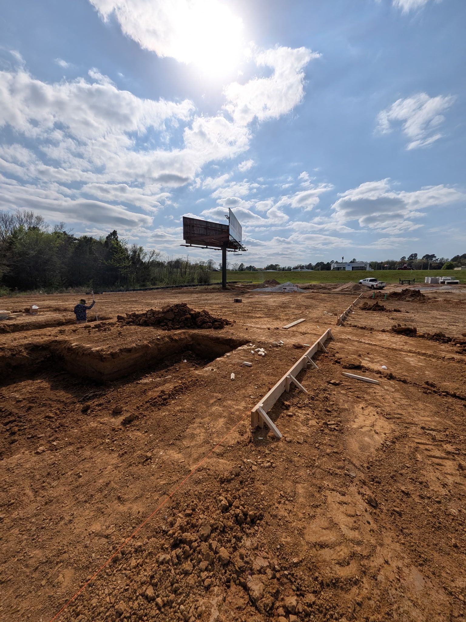 Dusty dirt lot with a leaning signpost, scattered debris, and a cloudy sky over distant trees.