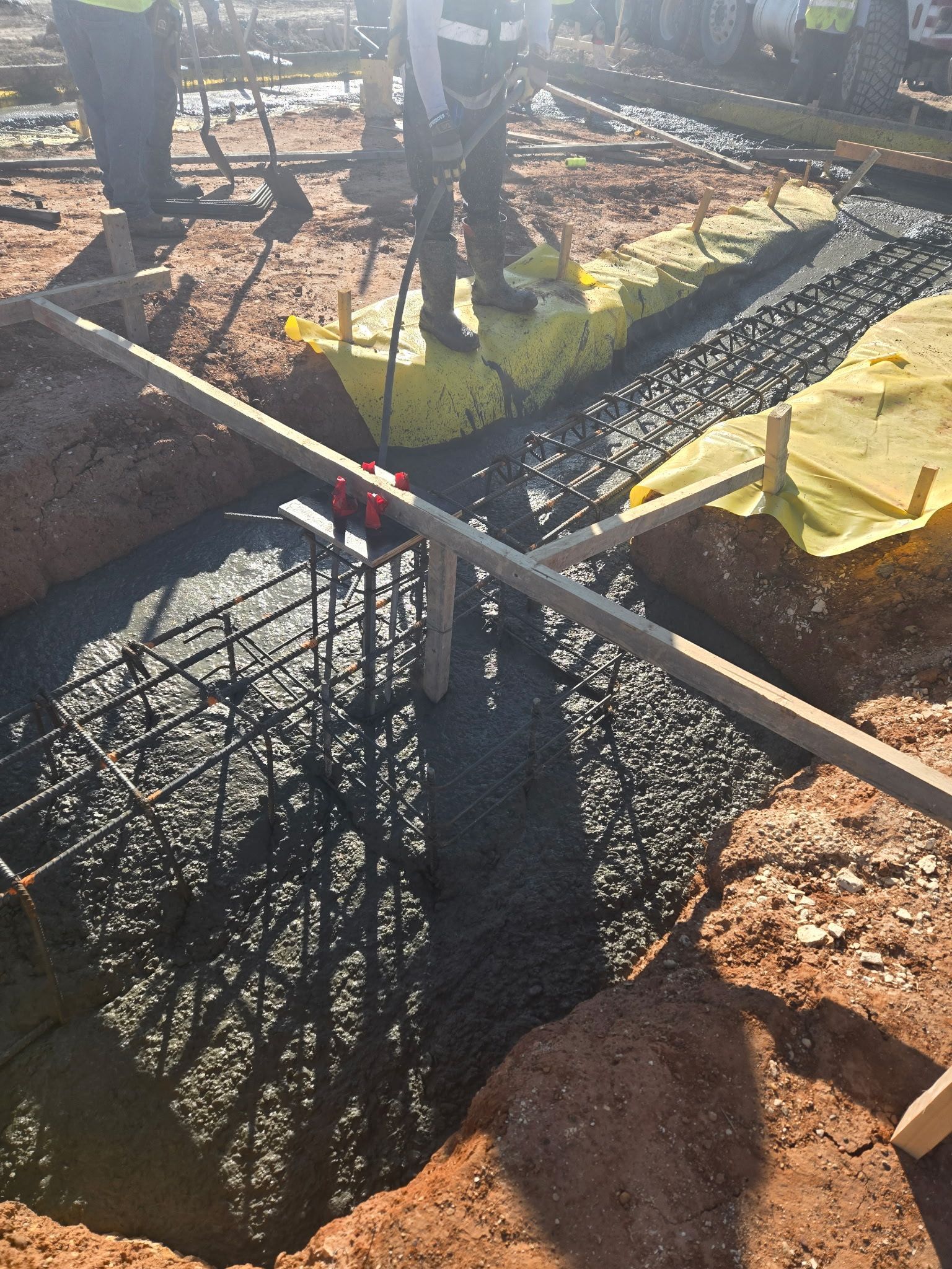 Concrete foundation forms with rebar and yellow tarp at a construction site