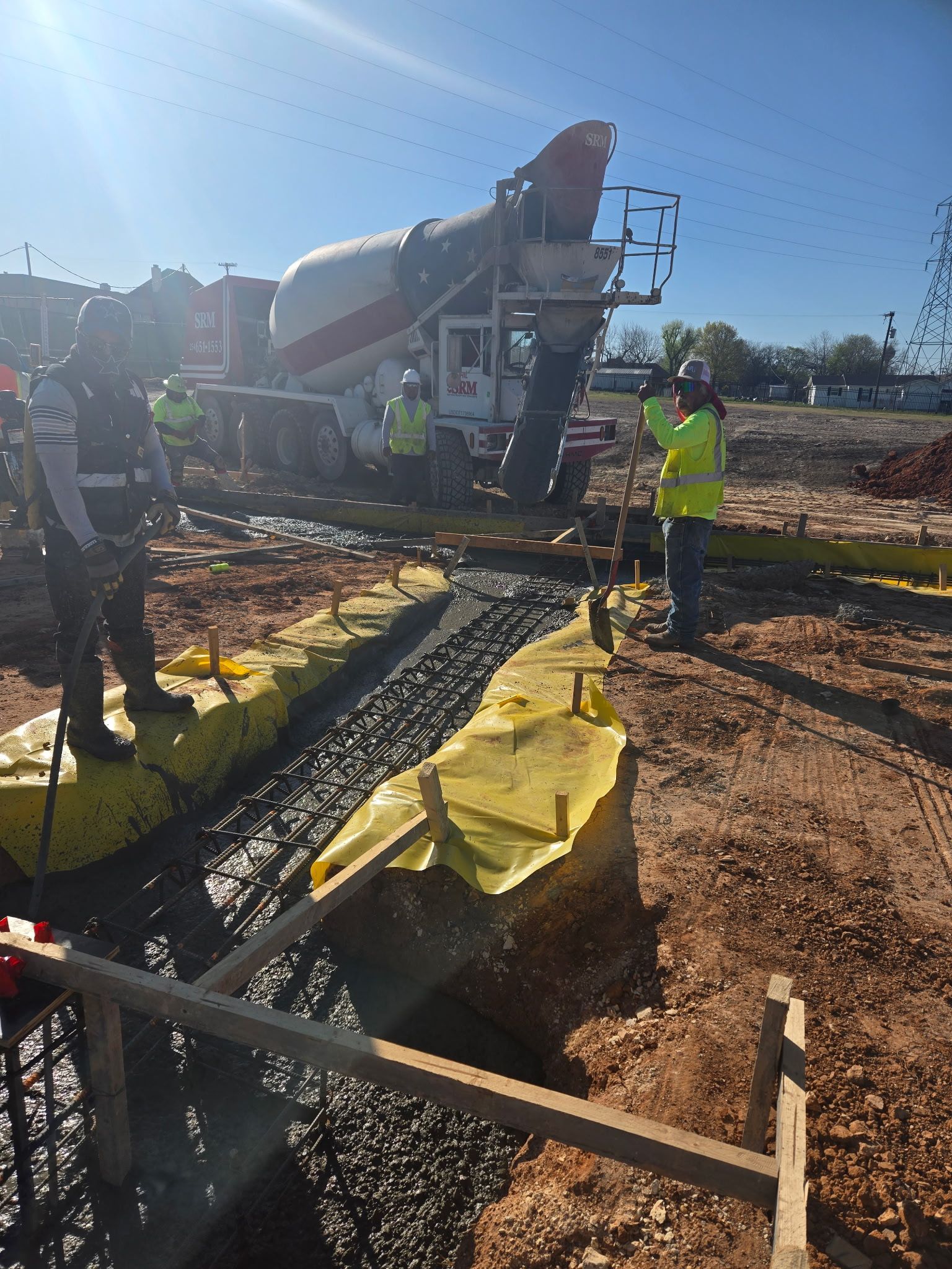 Construction workers pouring concrete from a mixer into a rebar-lined foundation trench