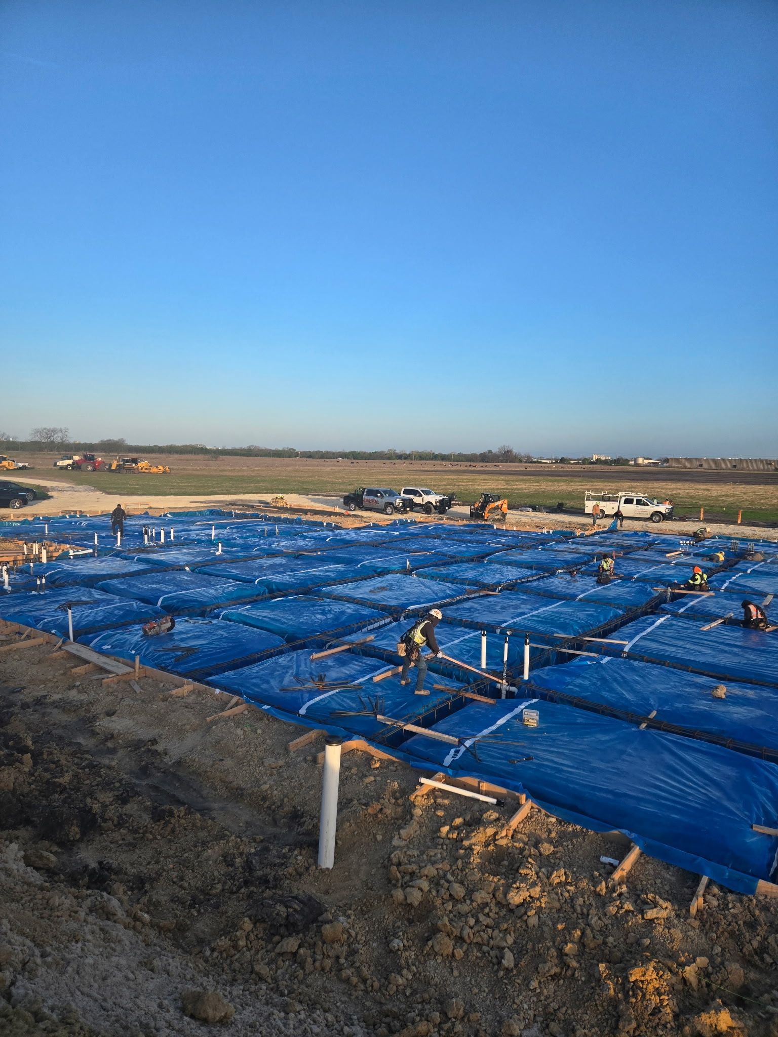 Blue tarps covering a large construction site under a clear sky, with workers and equipment in the distance