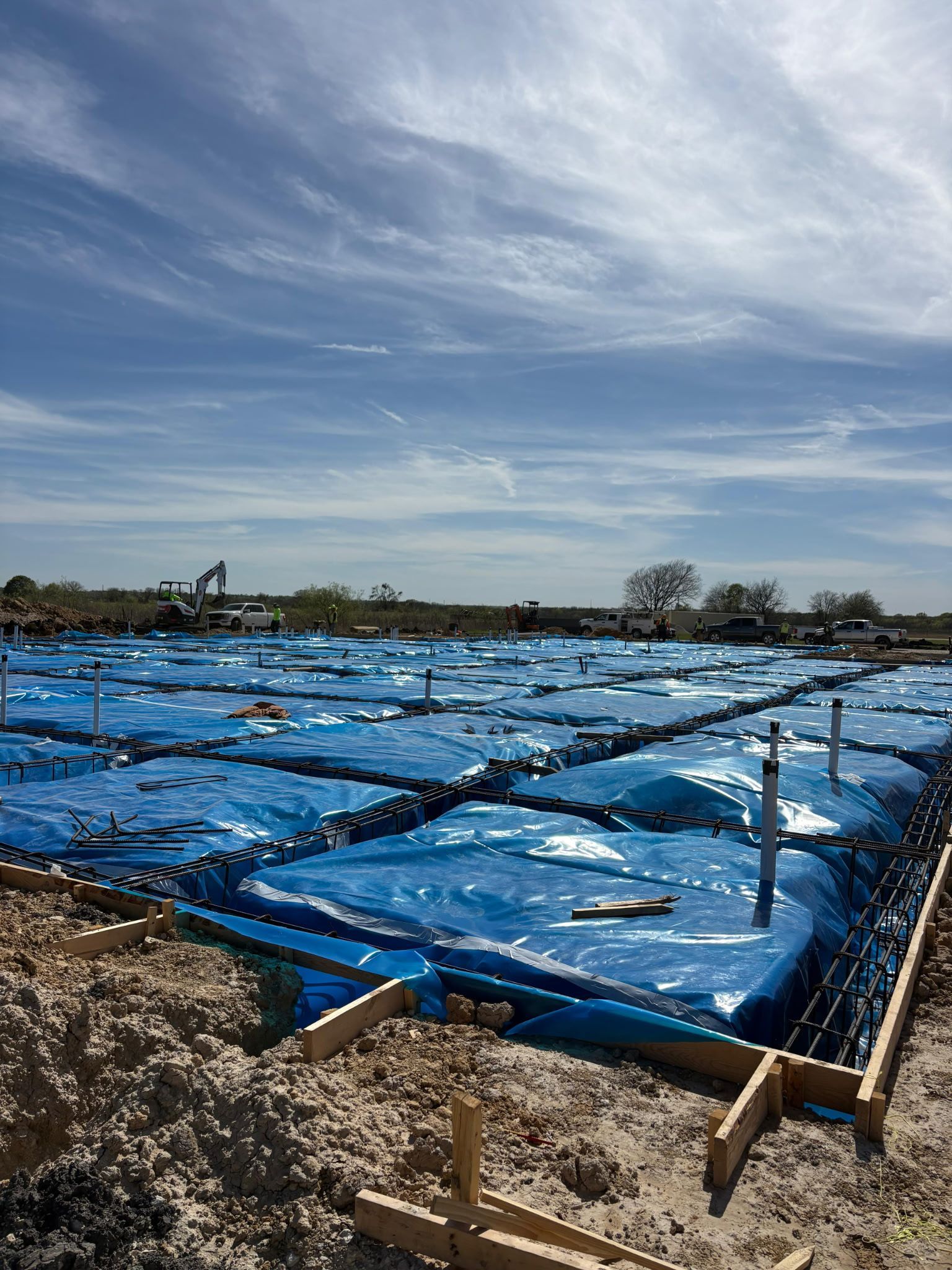 Blue tarped field with irrigation trenches under a cloudy sky, viewed from a rural roadside