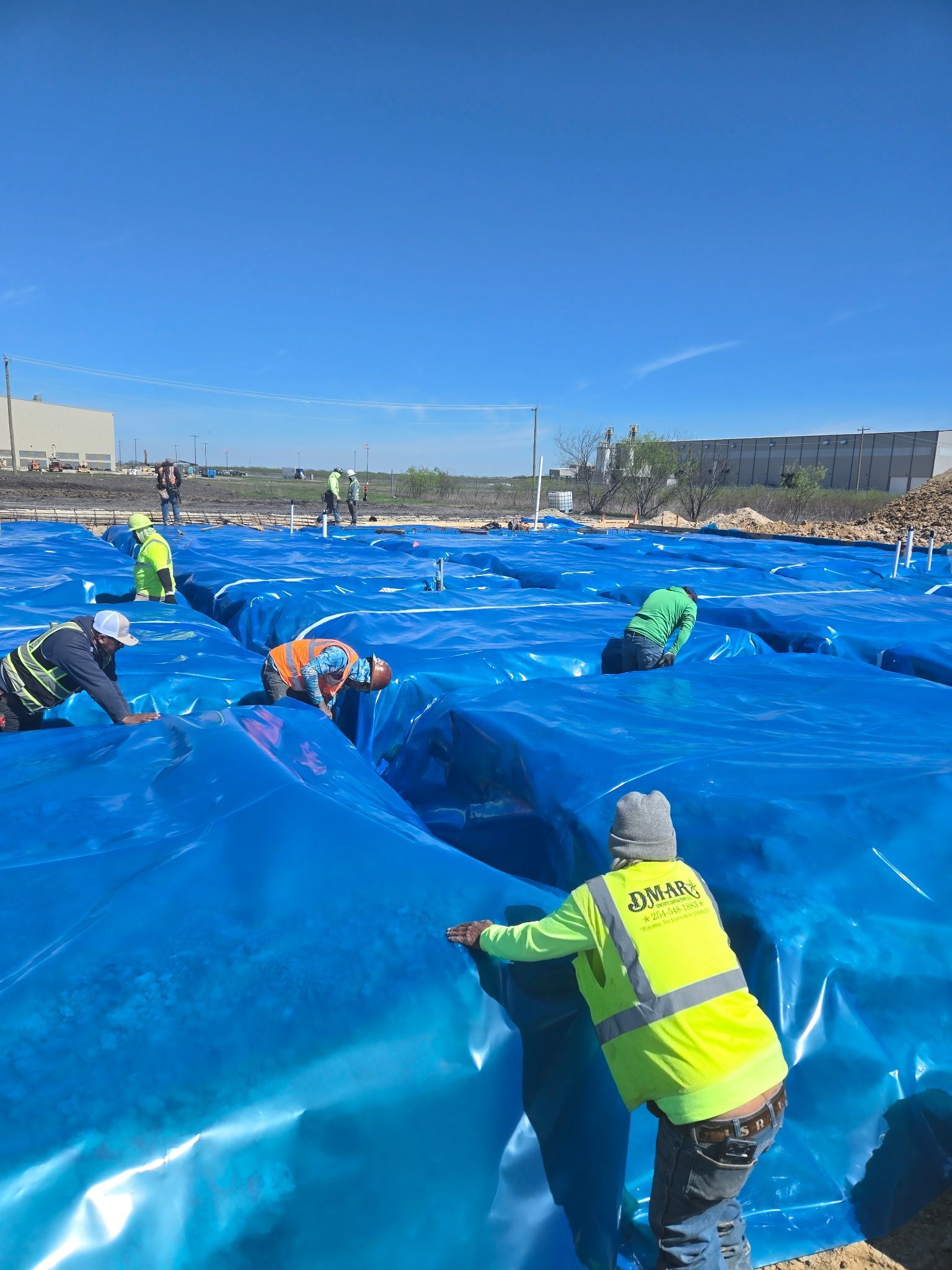 Volunteers in neon vests spreading a large blue tarp on a beach under a clear sky