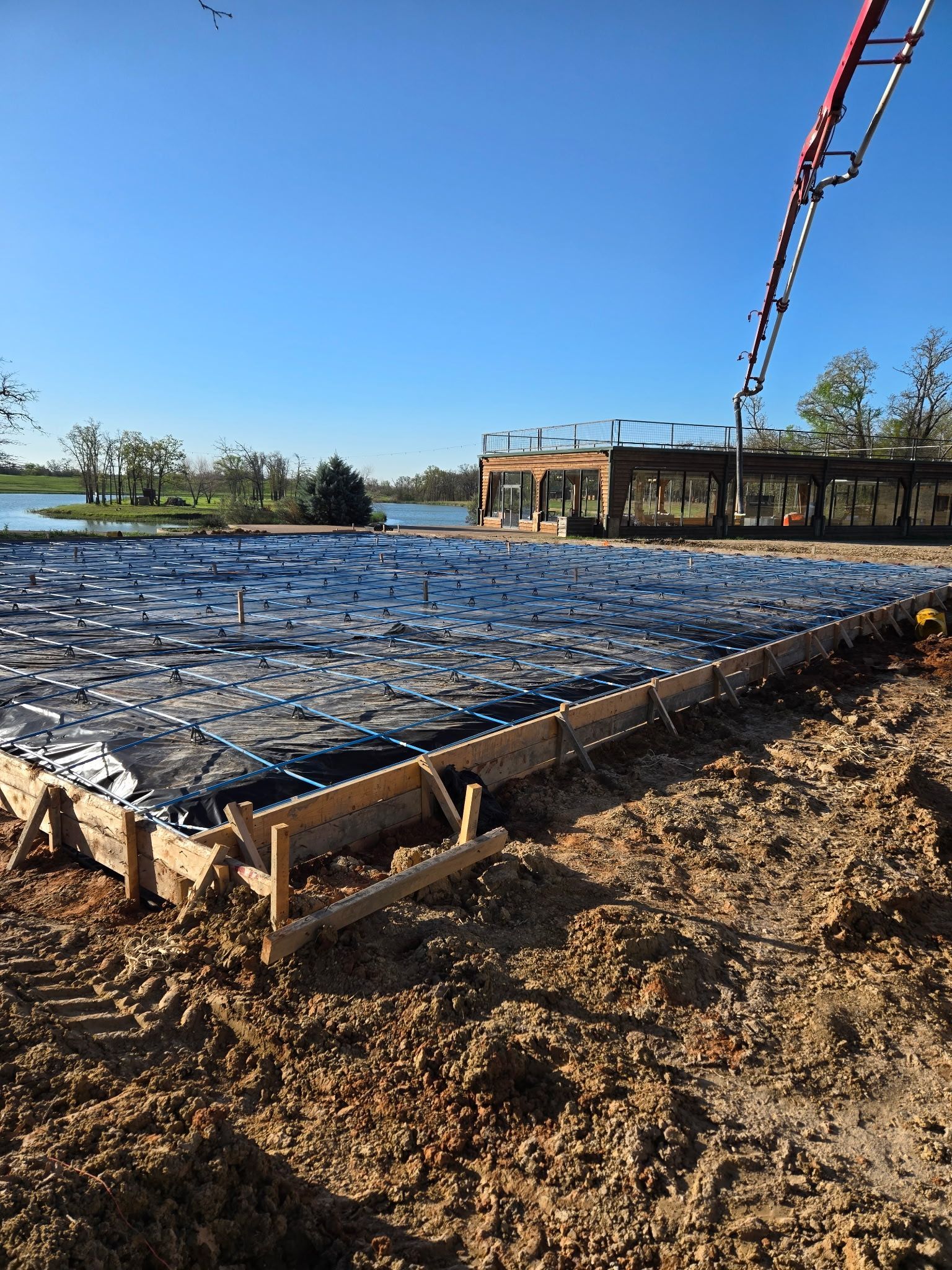 Reinforced concrete slab under construction with rebar grid, mud foreground, and blue sky overhead