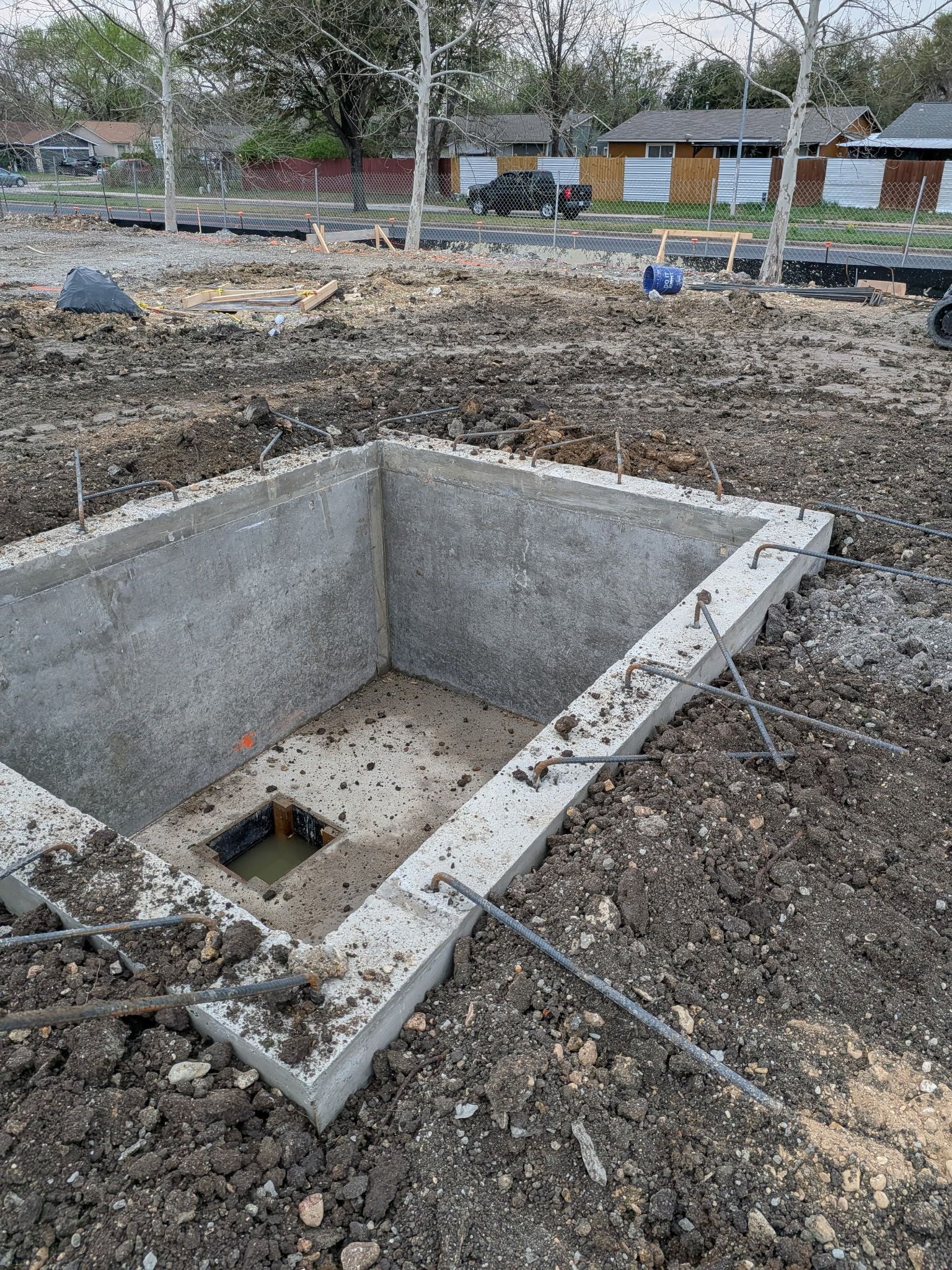 Concrete utility pit in a dirt lot with a small square opening and houses in the background