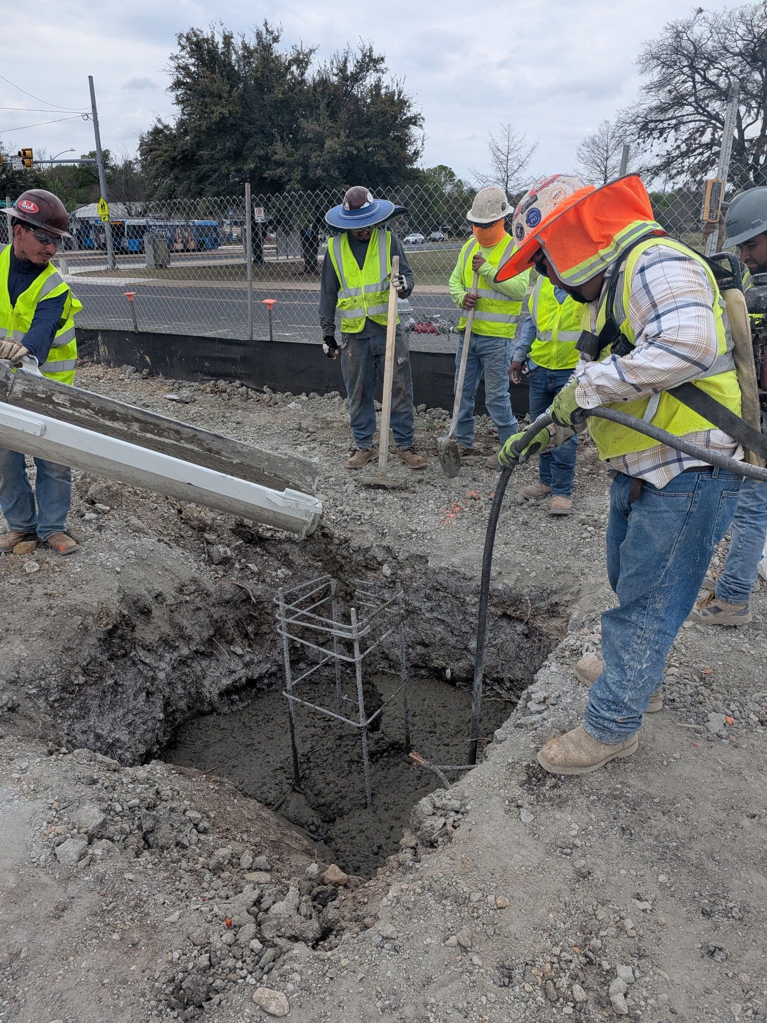 Construction workers in reflective gear repairing a large pothole on a road