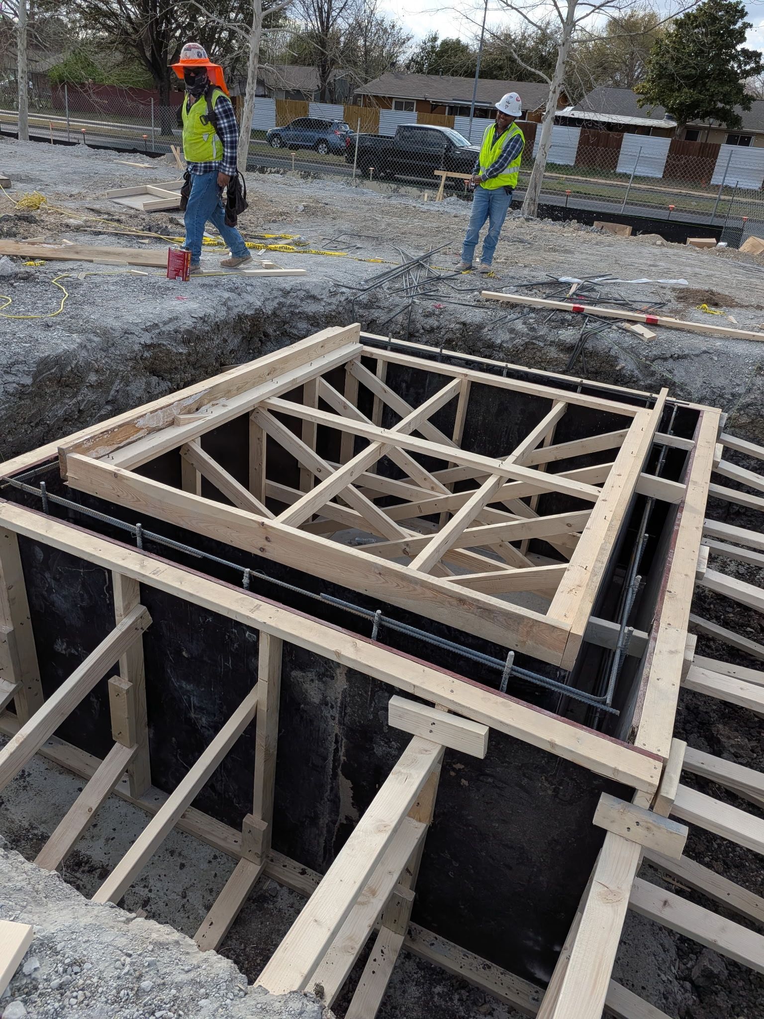 Workers in safety vests inspect a wooden formwork structure at a construction site.