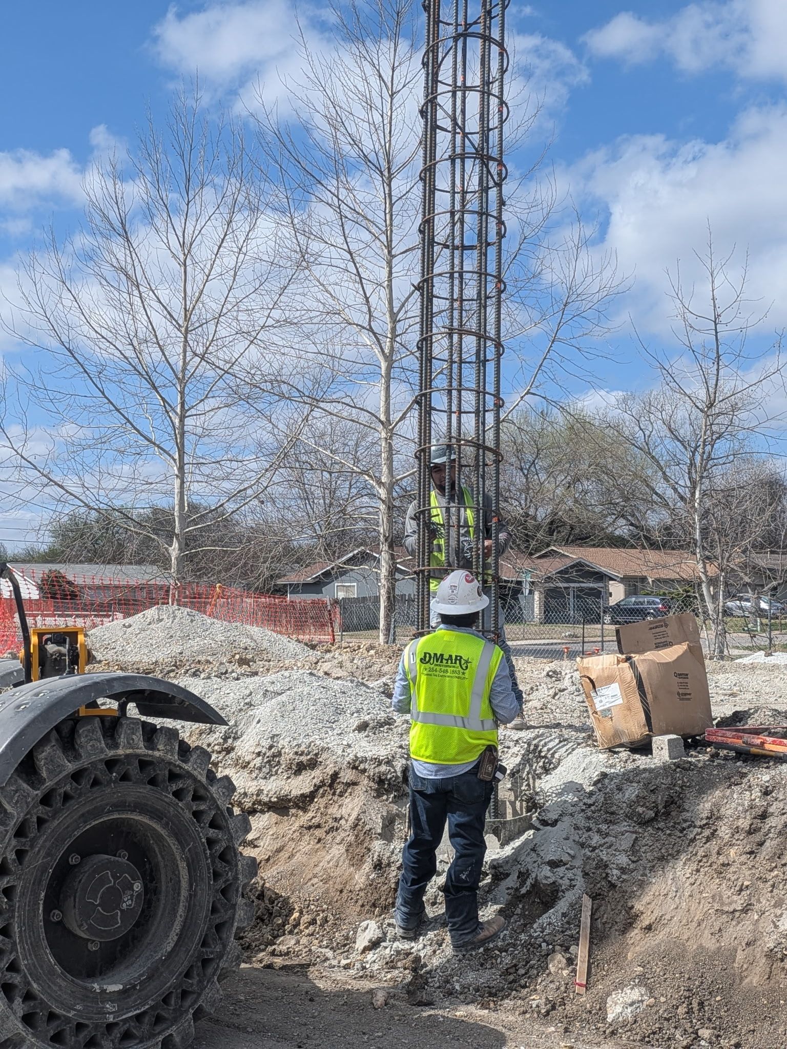 Construction worker in neon vest stands beside drilling rig at a roadwork site under a blue sky