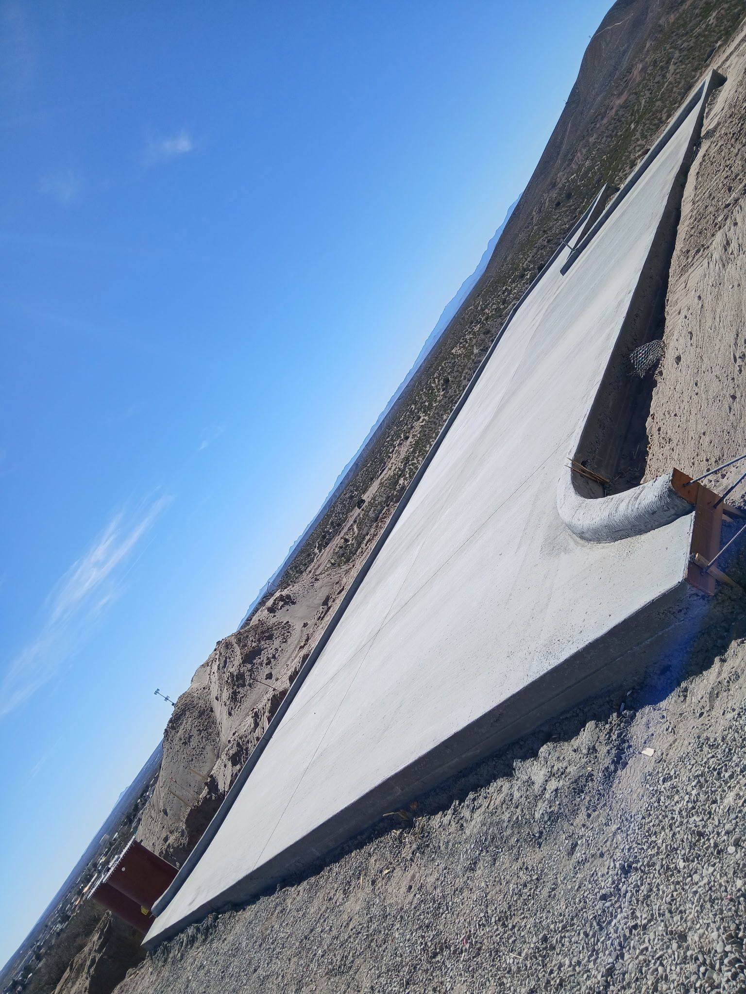 Tarp stretched over a gravel slope under a clear blue sky, held by a metal pipe.