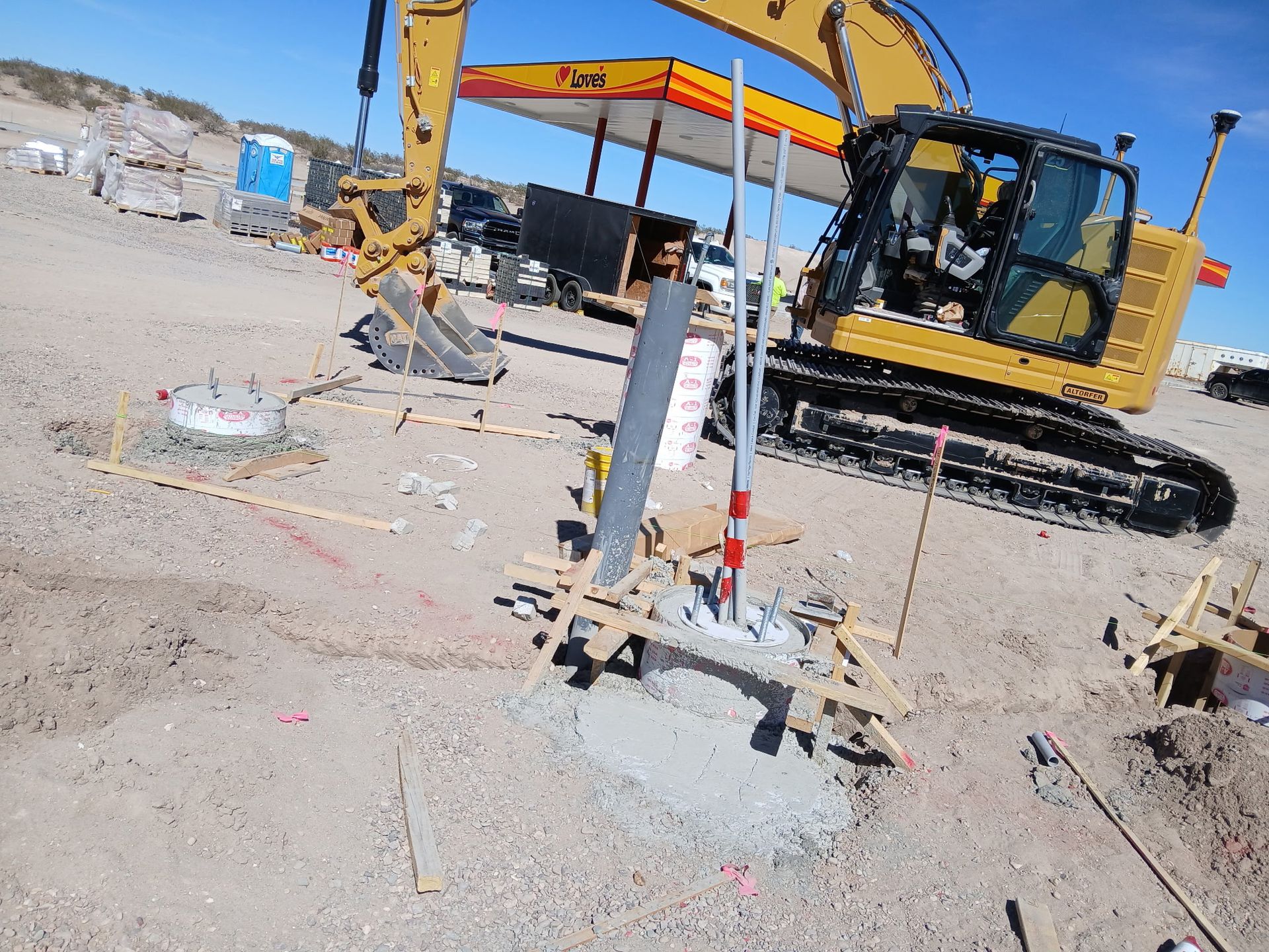 Yellow excavator working on a dusty construction site with pipes and gravel, near a small canopy shelter