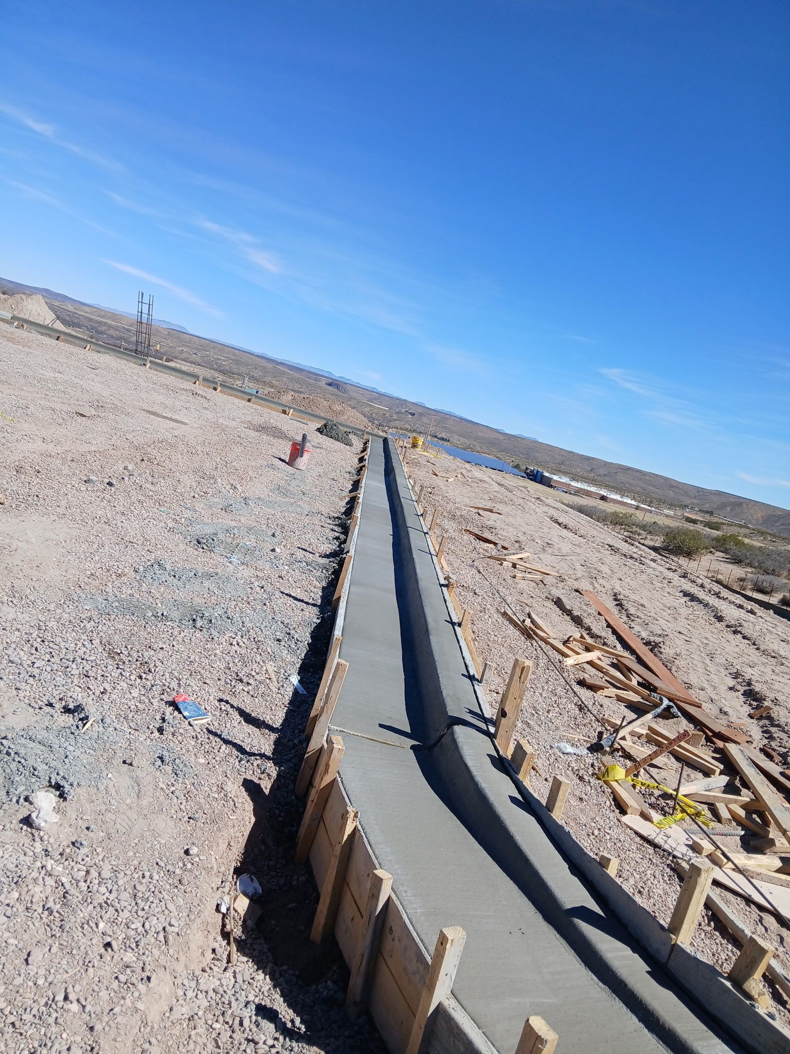 Concrete irrigation channel under construction across a rocky desert landscape beneath a blue sky