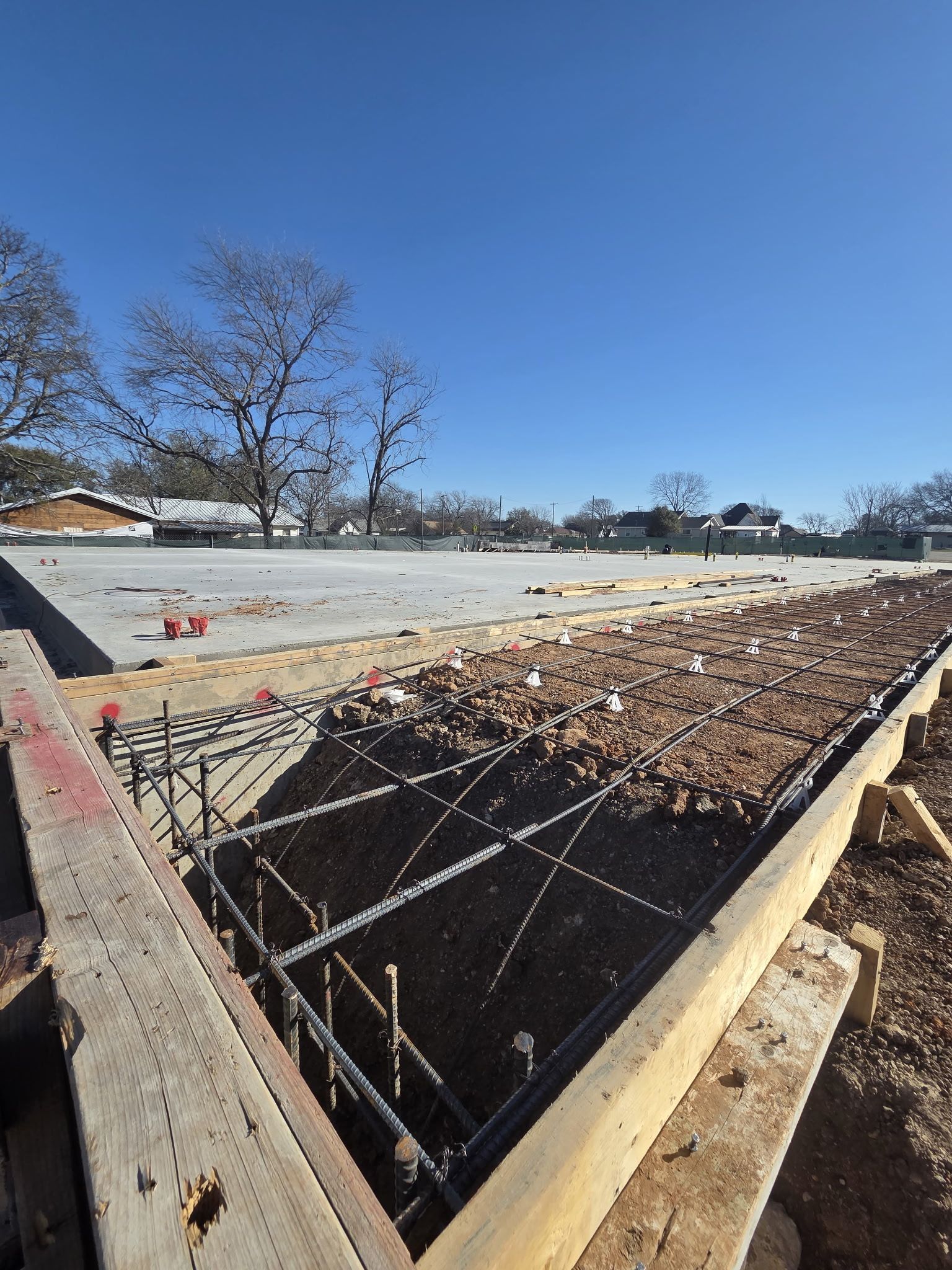 Concrete foundation with exposed rebar and fallen leaves under a clear blue sky