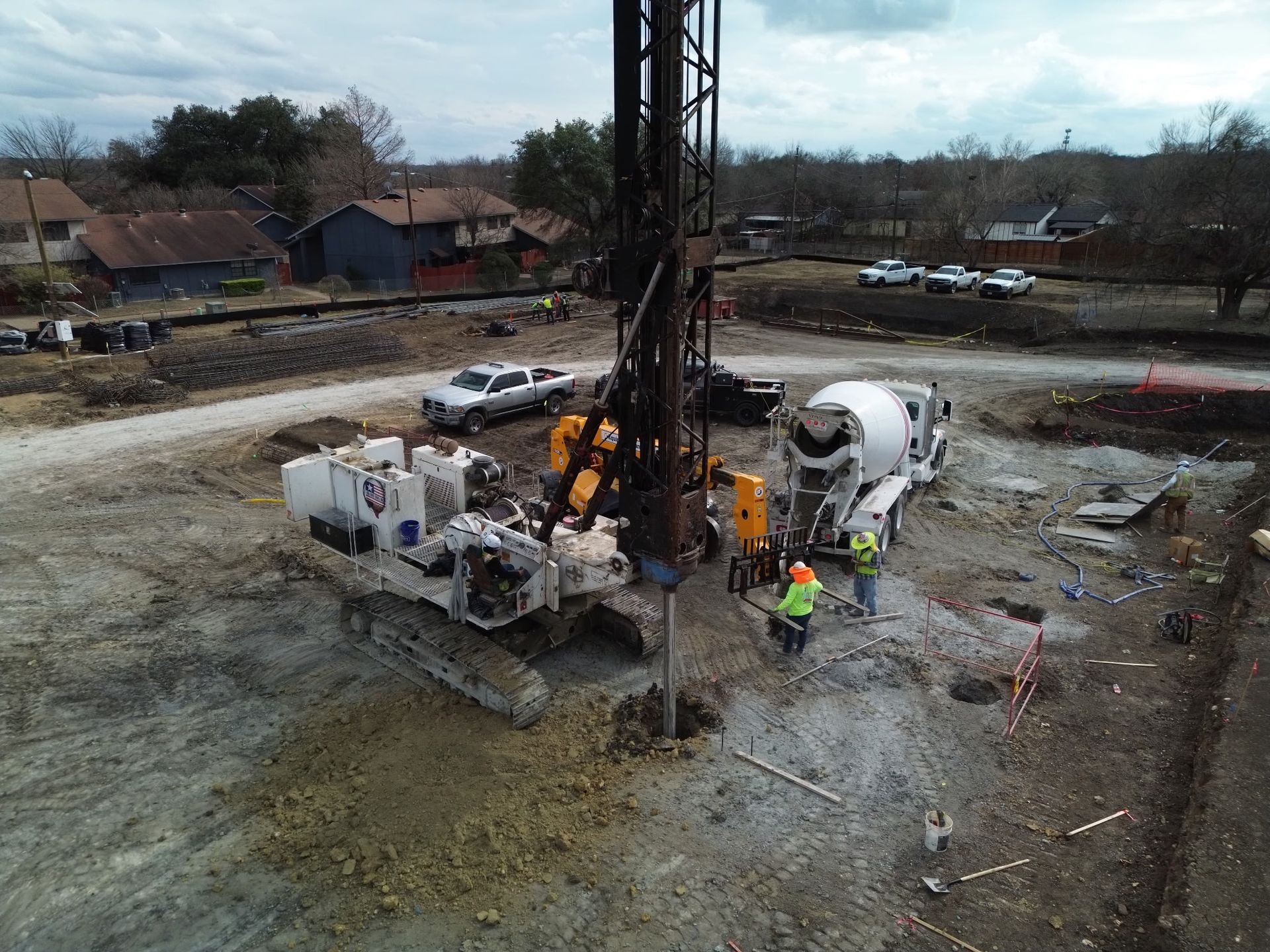 Concrete drilling rig at a muddy construction site with workers and trucks nearby