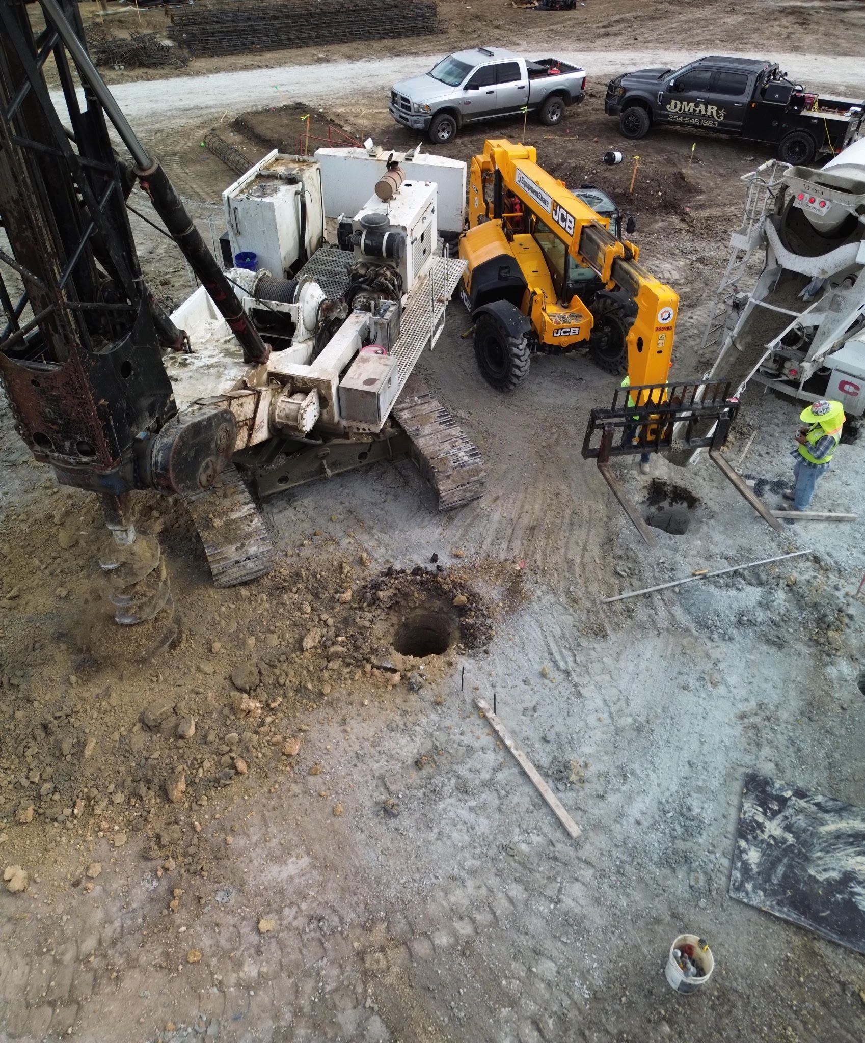 Construction site with yellow crane and excavator beside a concrete structure and parked truck.