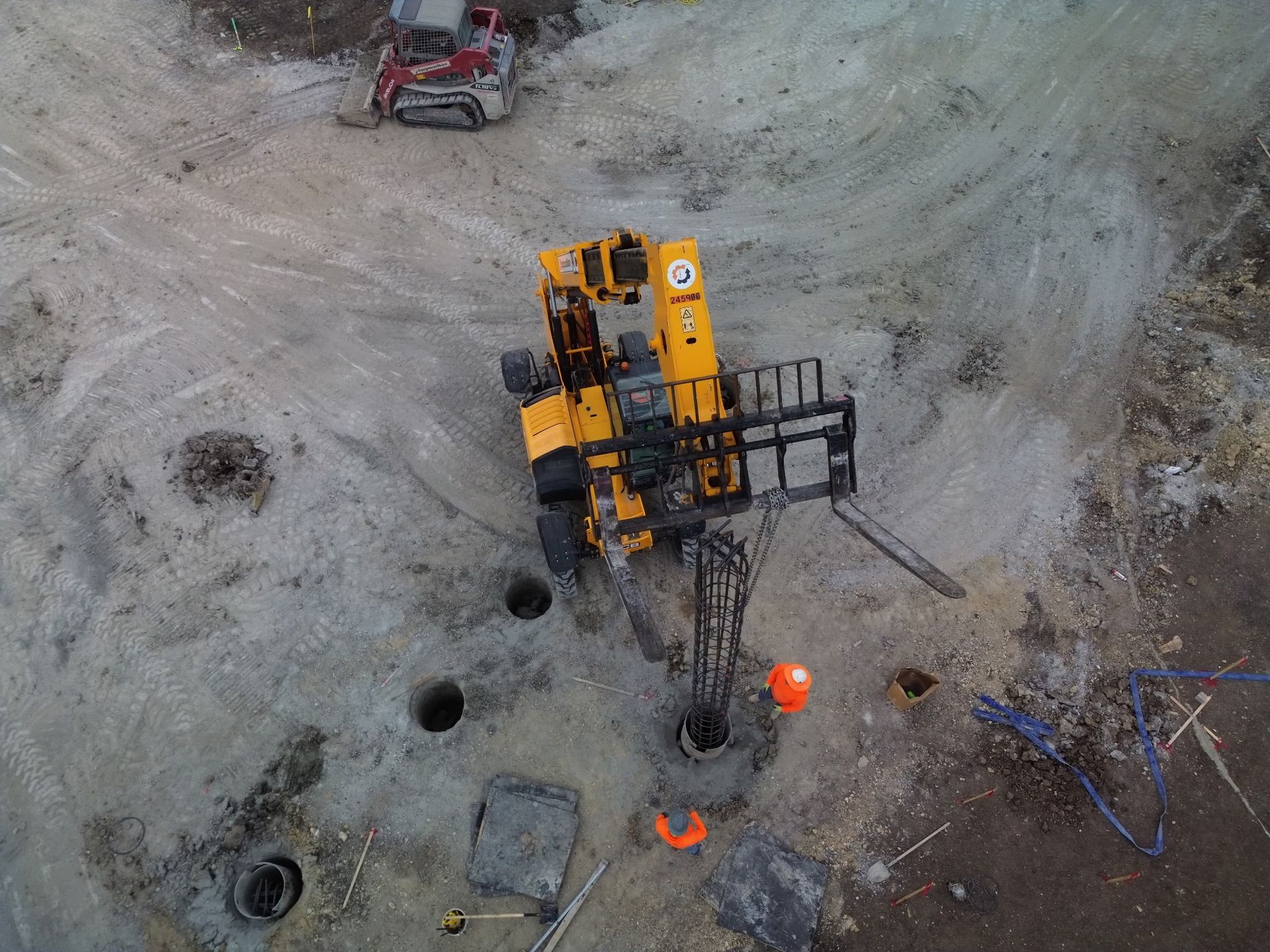 Aerial view of a yellow drilling rig at a construction site with workers and equipment nearby.