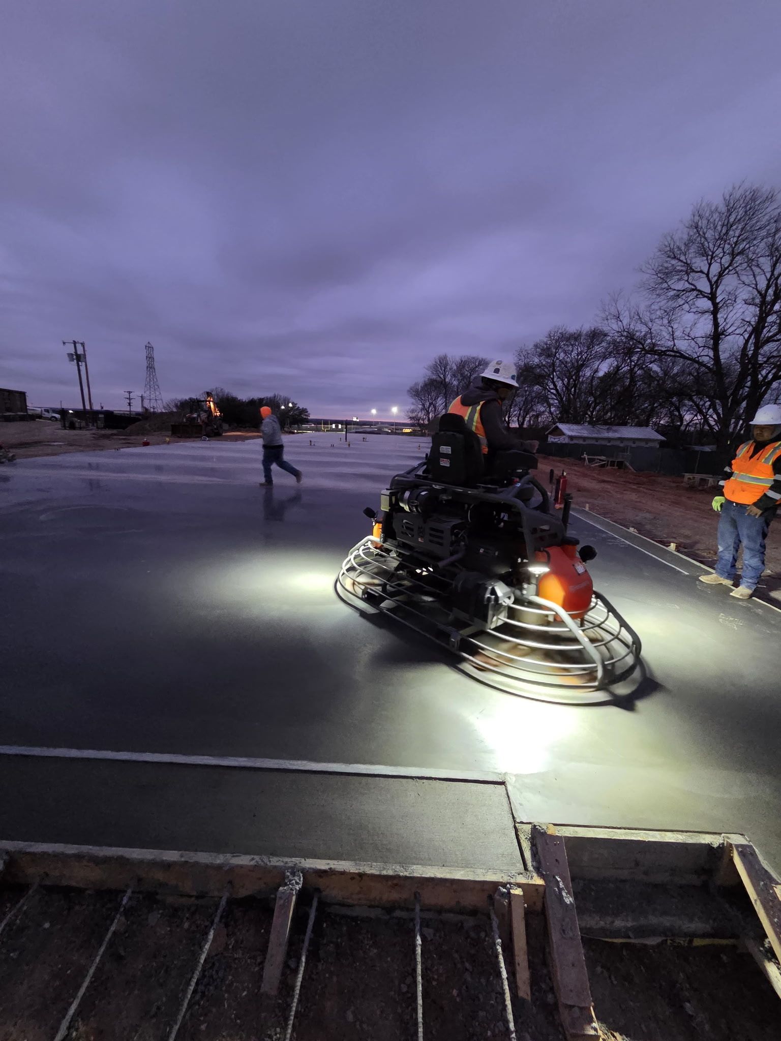 Snowmobile on wet pavement at dusk, with people in reflective jackets nearby.