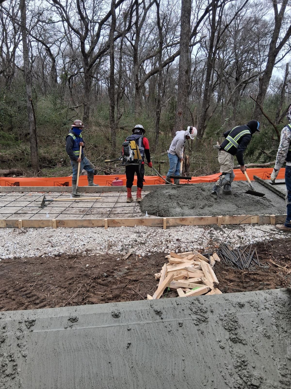 Workers pour concrete for a foundation at a construction site in a wooded area.