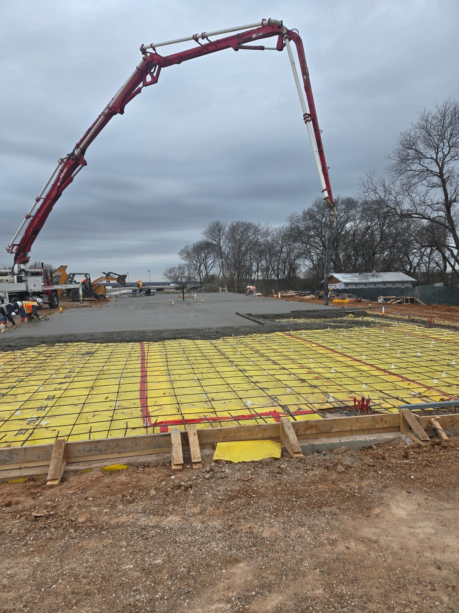 Concrete pump boom pouring over a large construction site under an overcast sky