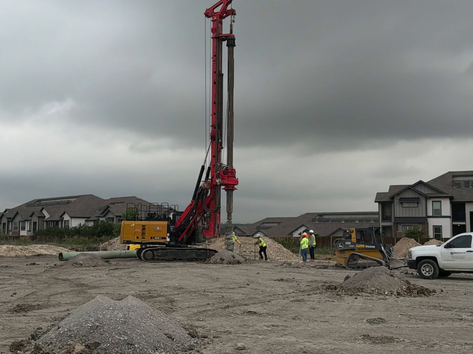 Construction site with tall red drilling rig, workers, and cloudy sky in a new neighborhood