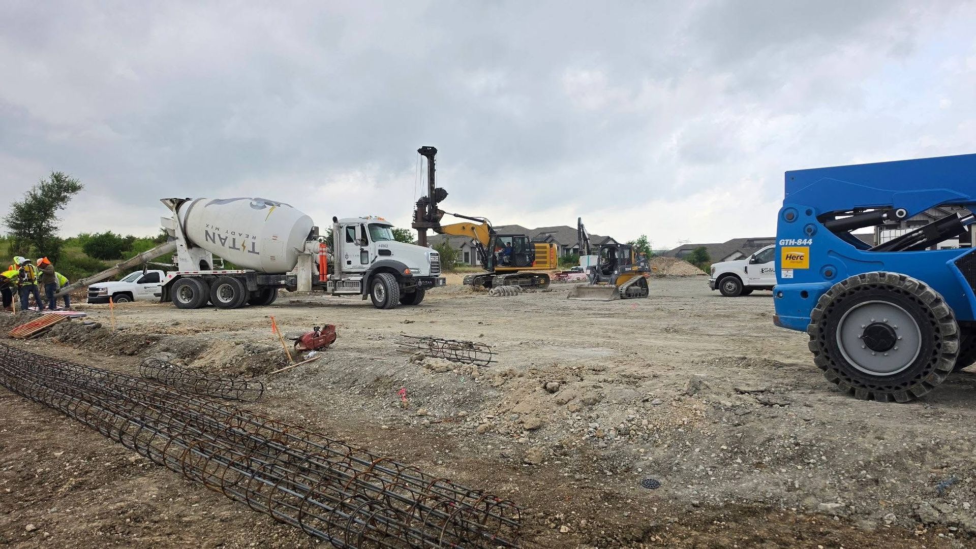 Construction site with cement mixer truck, excavator, and blue loader on gravel under cloudy sky