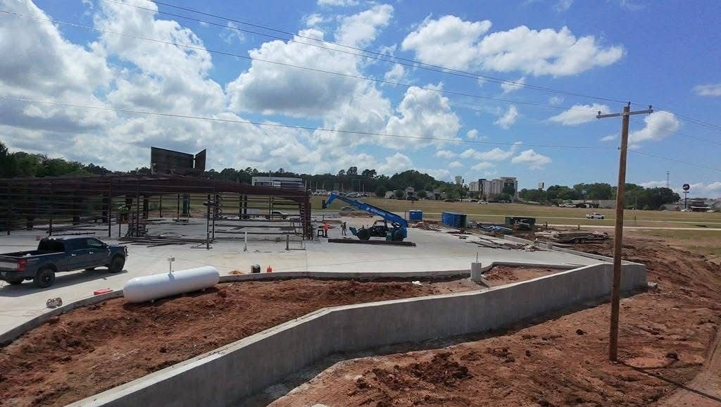 Road construction site with curving concrete curb, dirt piles, trucks, and cloudy sky