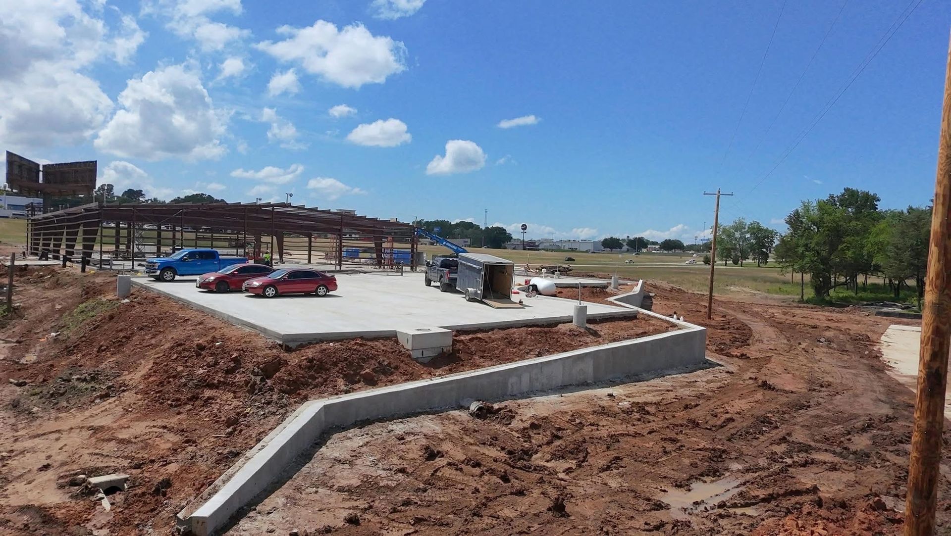 Construction site with concrete foundation, dirt roads, and blue sky on a sunny day