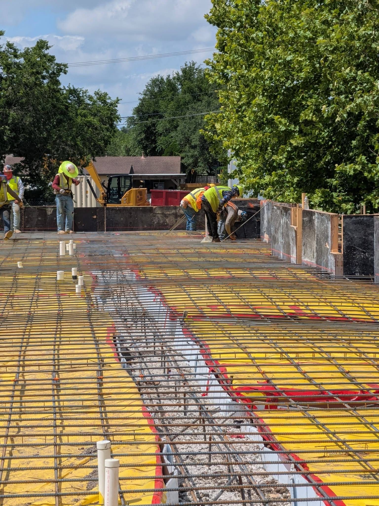 Concrete bridge deck under construction with rebar, workers, and trees in the background