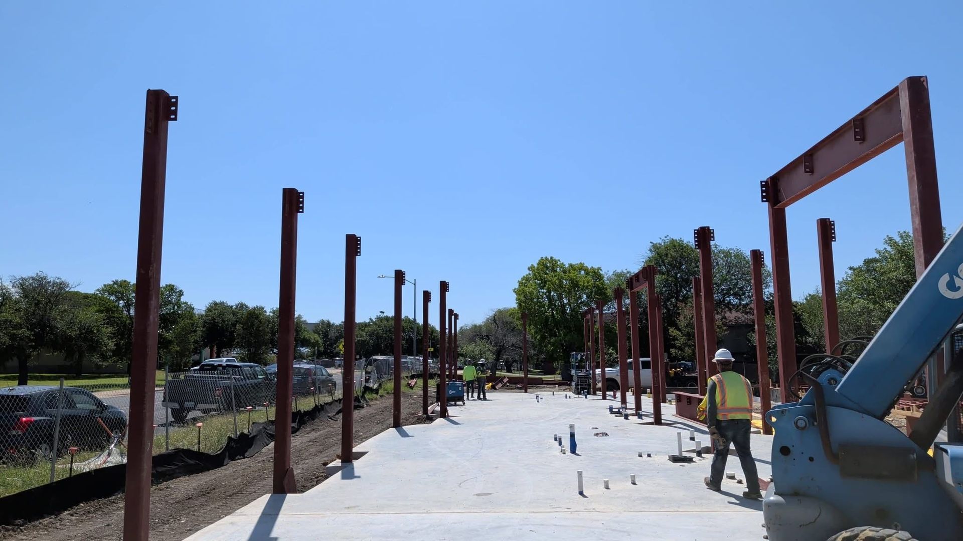 Construction workers installing metal posts along a concrete path under a bright blue sky