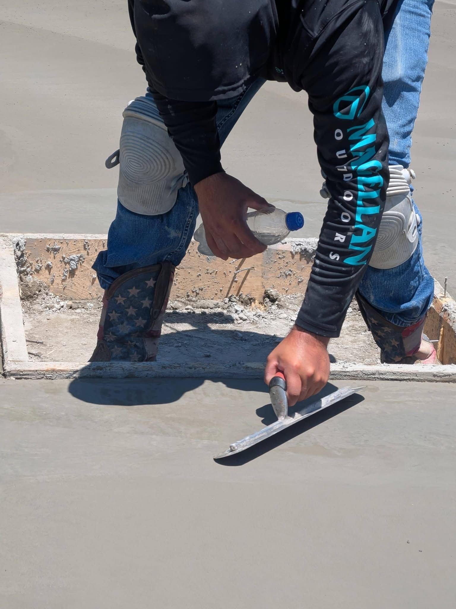 Worker smoothing wet concrete with a trowel on a sidewalk slab