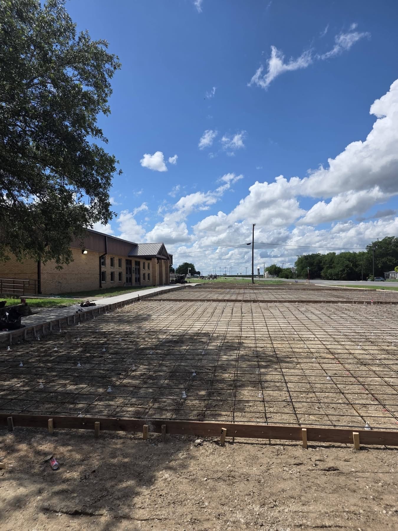 Empty concrete lot beside a brick building under a blue sky with scattered clouds.