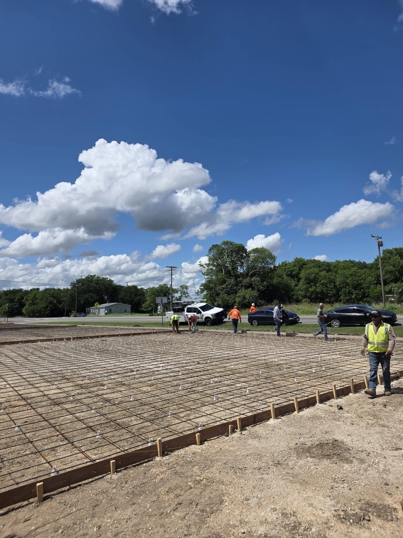 Workers pour a concrete slab at a construction site under a blue sky.