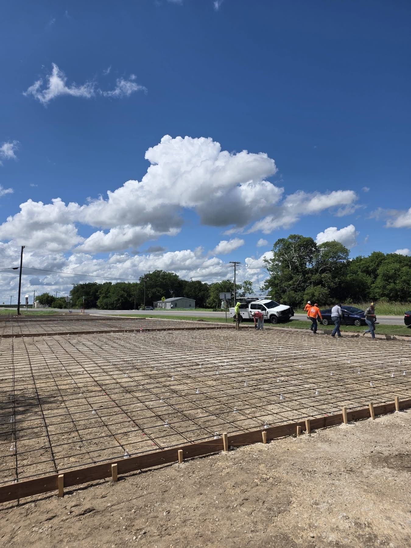 Concrete slab construction site under a blue sky, with workers, a truck, and forms in place
