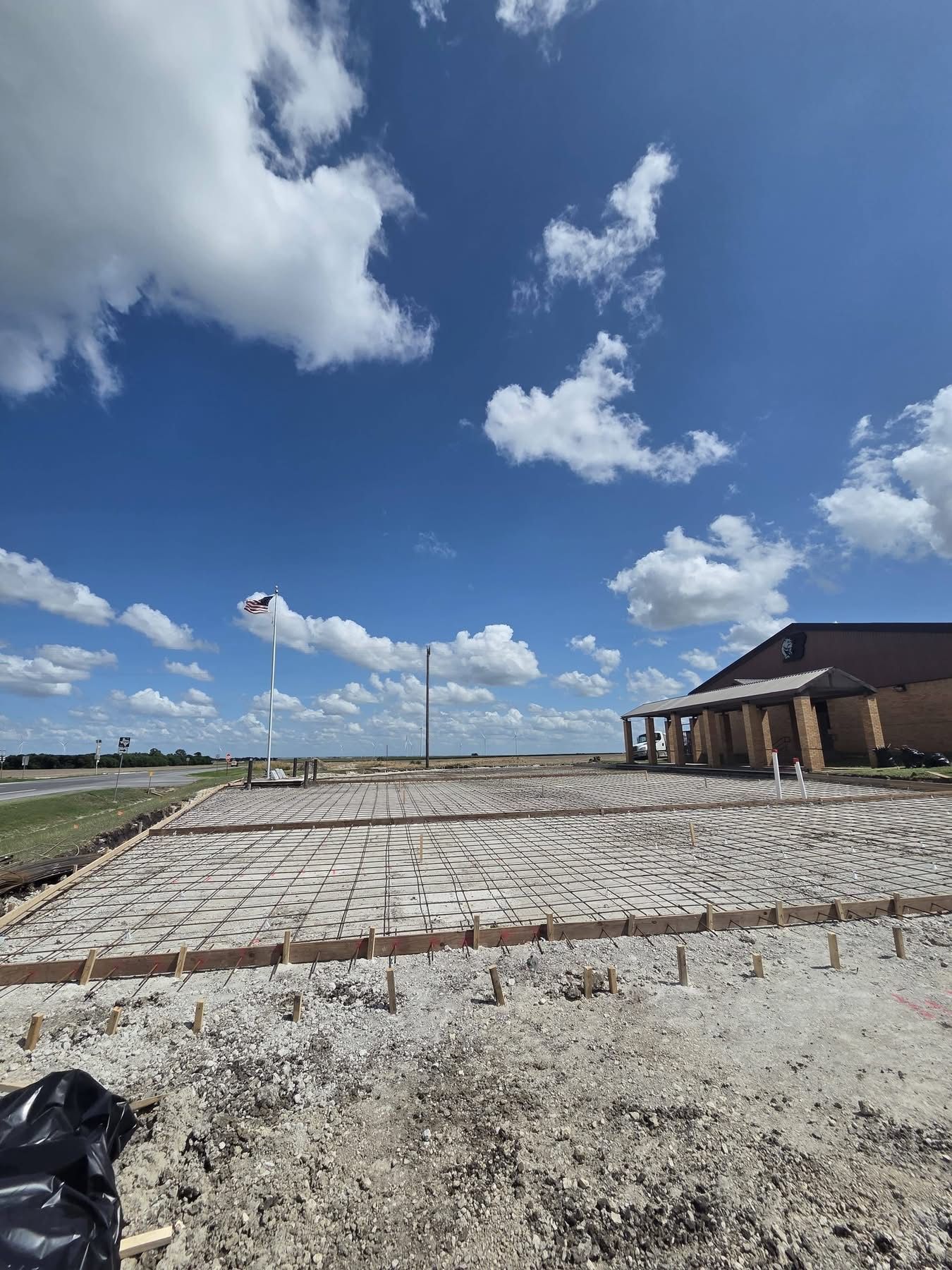 Wide stone courtyard under a bright blue sky with scattered clouds and a building on the right