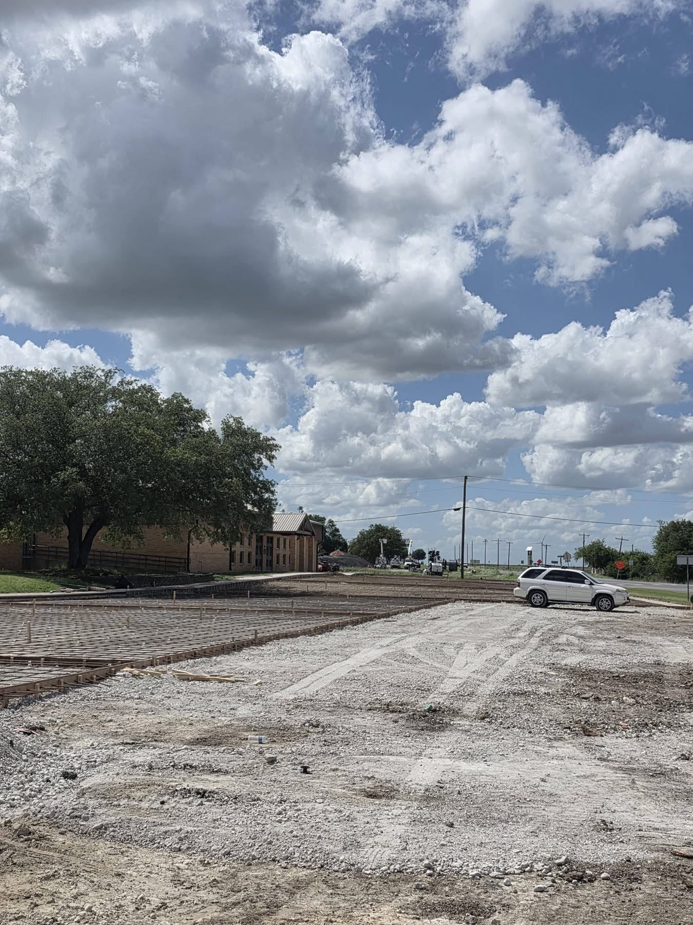 A gravel lot beside trees and a building, with a white truck under a cloudy sky.