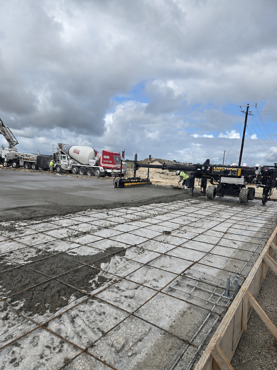 Construction site with concrete slab, trucks, and workers under cloudy sky
