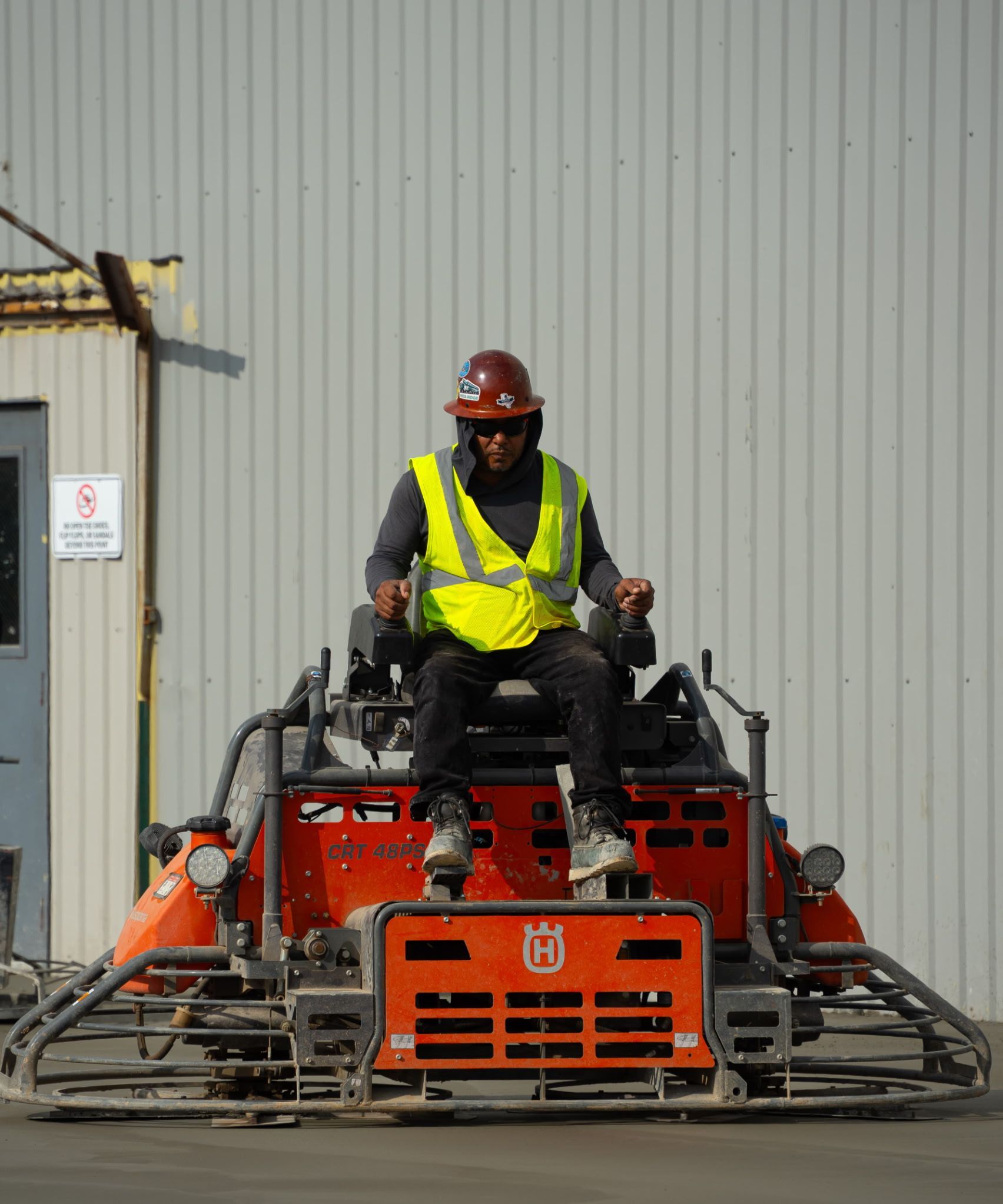 Worker in neon safety vest and hard hat operating a red construction machine outdoors.