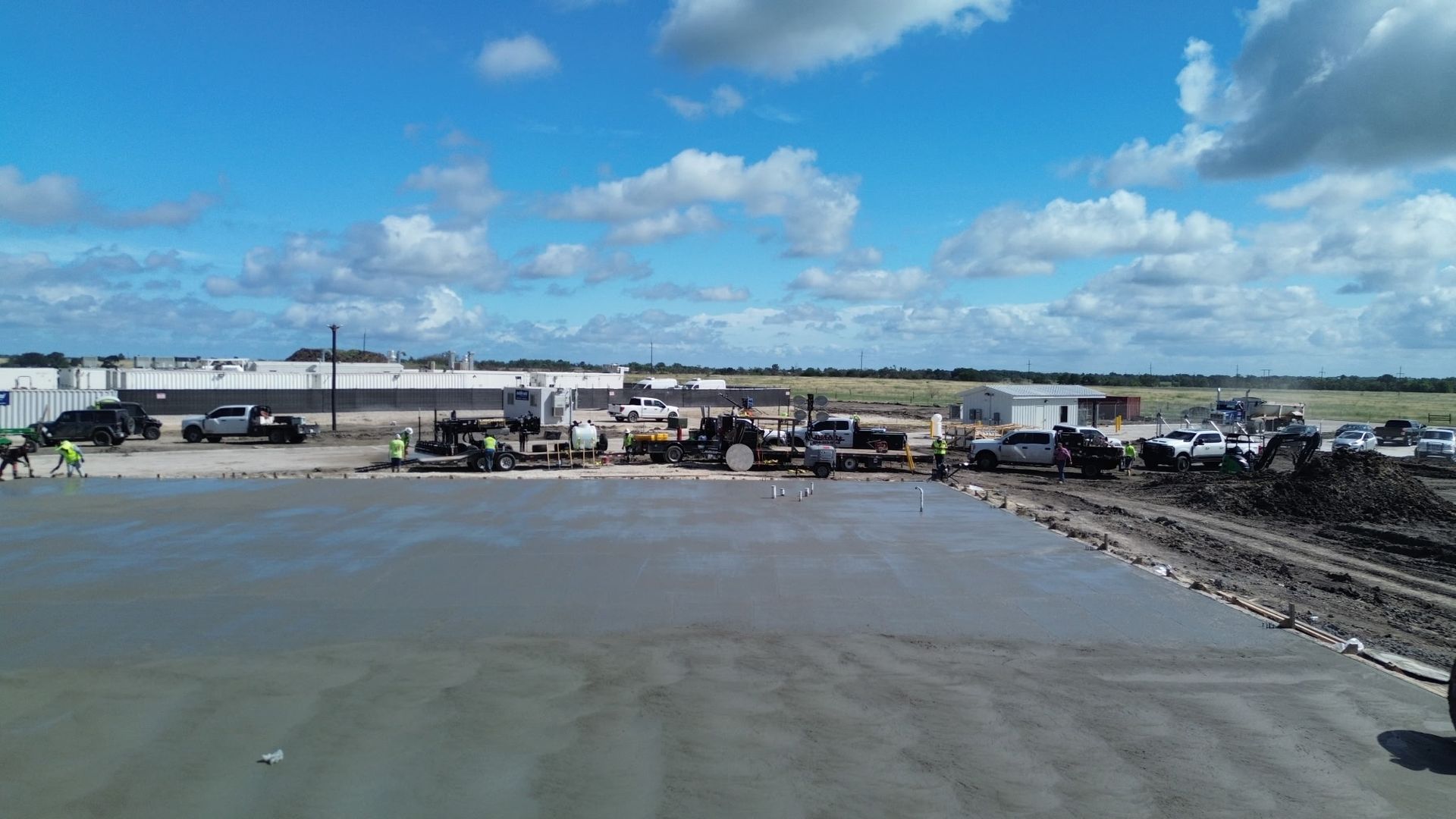 Wide construction site beside a runway under a blue sky with clouds