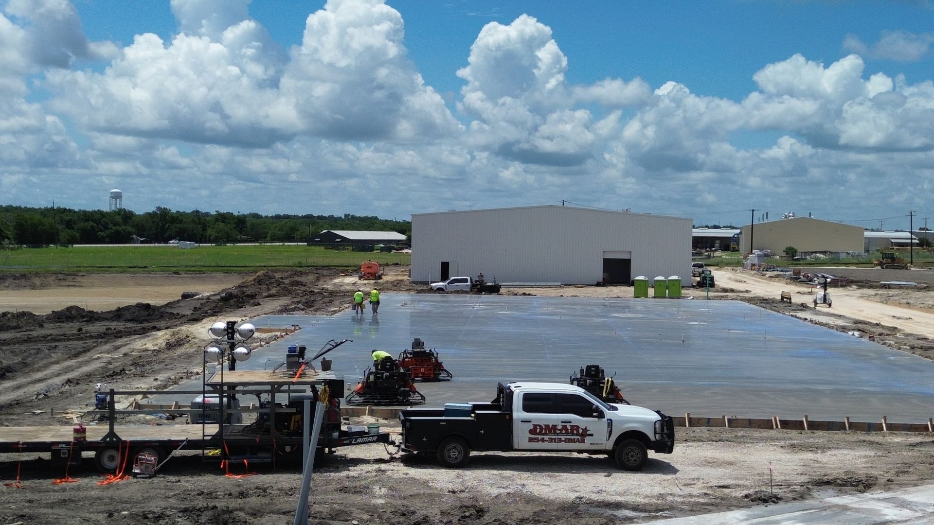 Construction site with concrete slab, workers, and white pickup trucks under a cloudy sky
