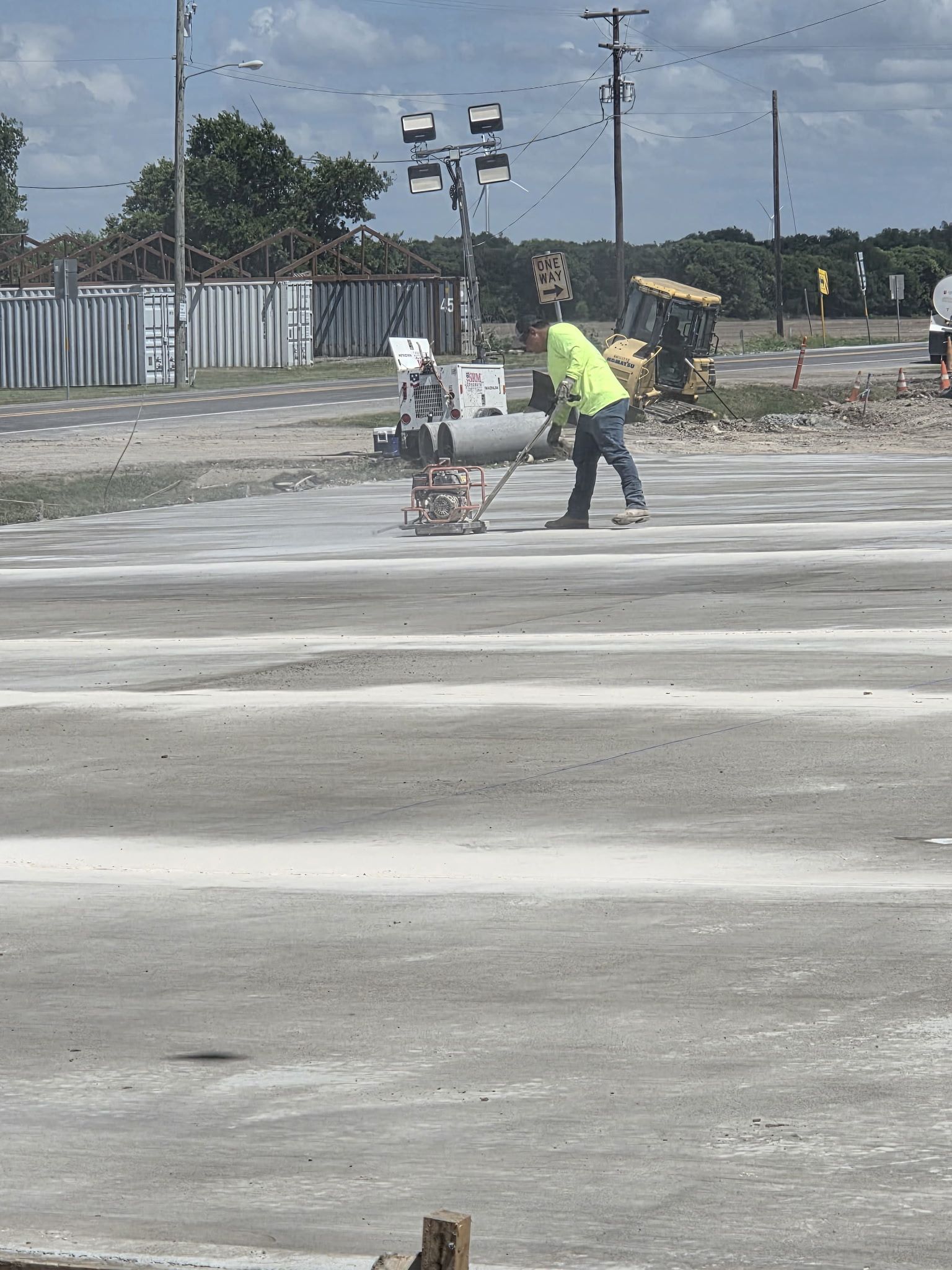 Workers paving a concrete lot with construction equipment under a cloudy sky