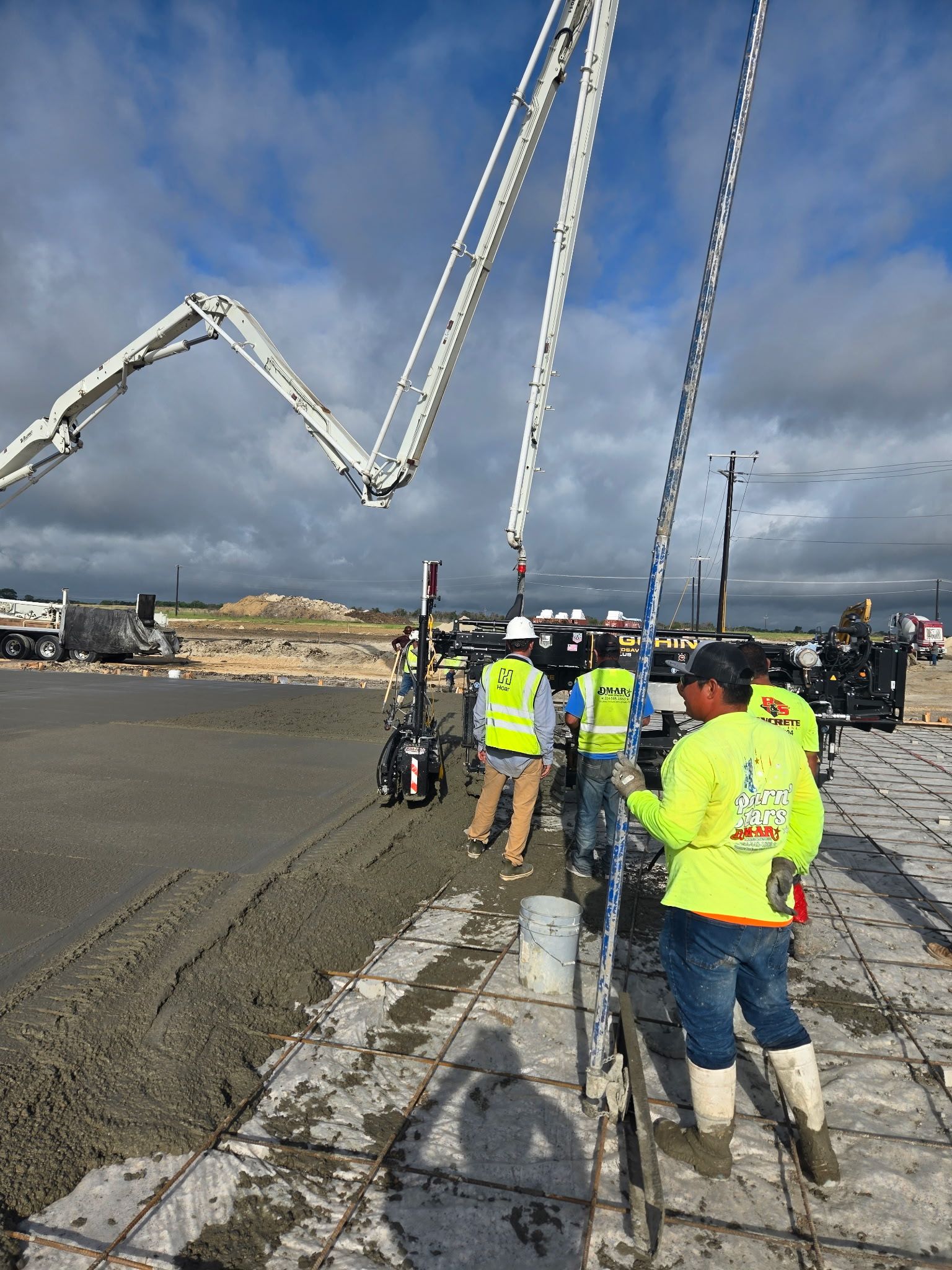 Workers in high-visibility gear on a construction site with a concrete pump boom overhead.