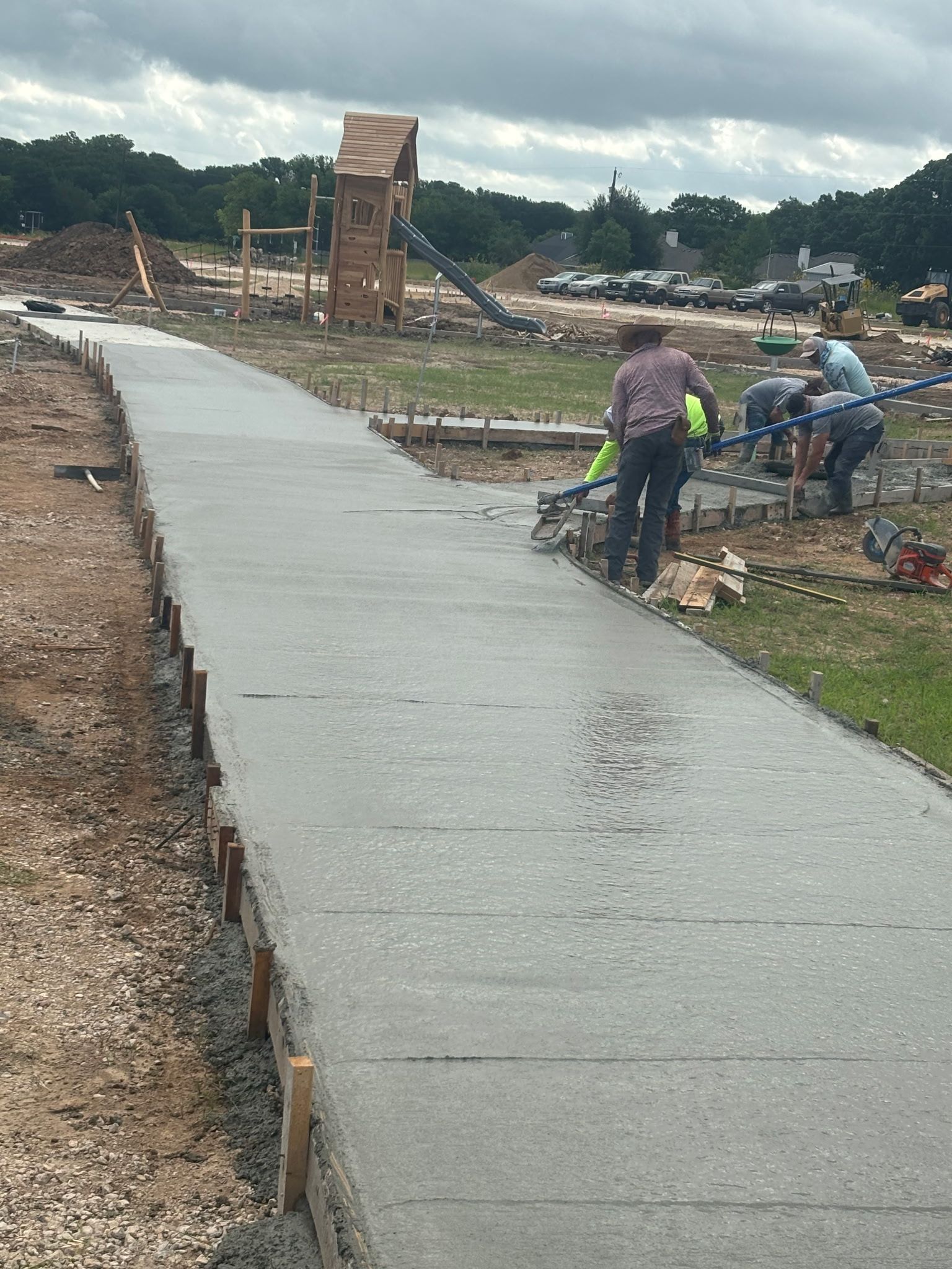 Freshly poured concrete walkway under construction with workers and materials along the sides