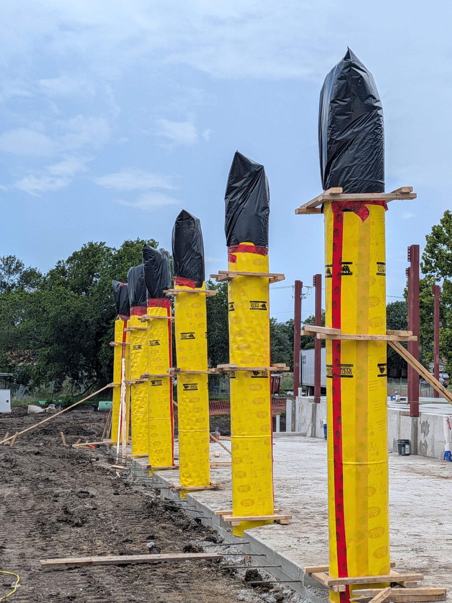 Row of yellow posts with black wrapped tops on a construction site under a blue sky