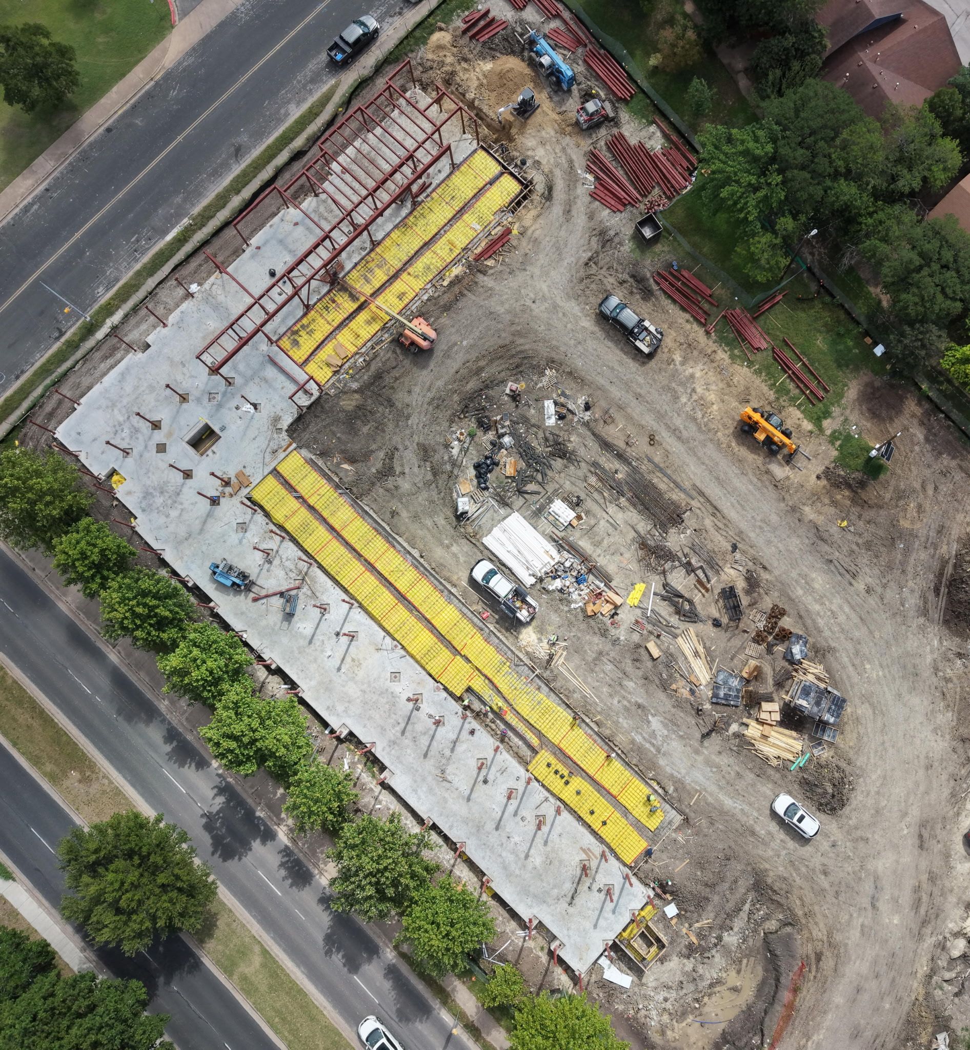 Aerial view of a construction site with concrete slabs, yellow materials, and parked equipment beside a road.